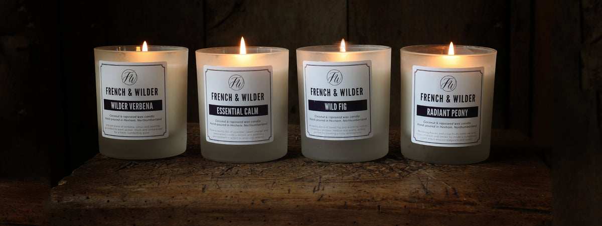 Four candles from French & Wilder on a wooden surface with a dark background