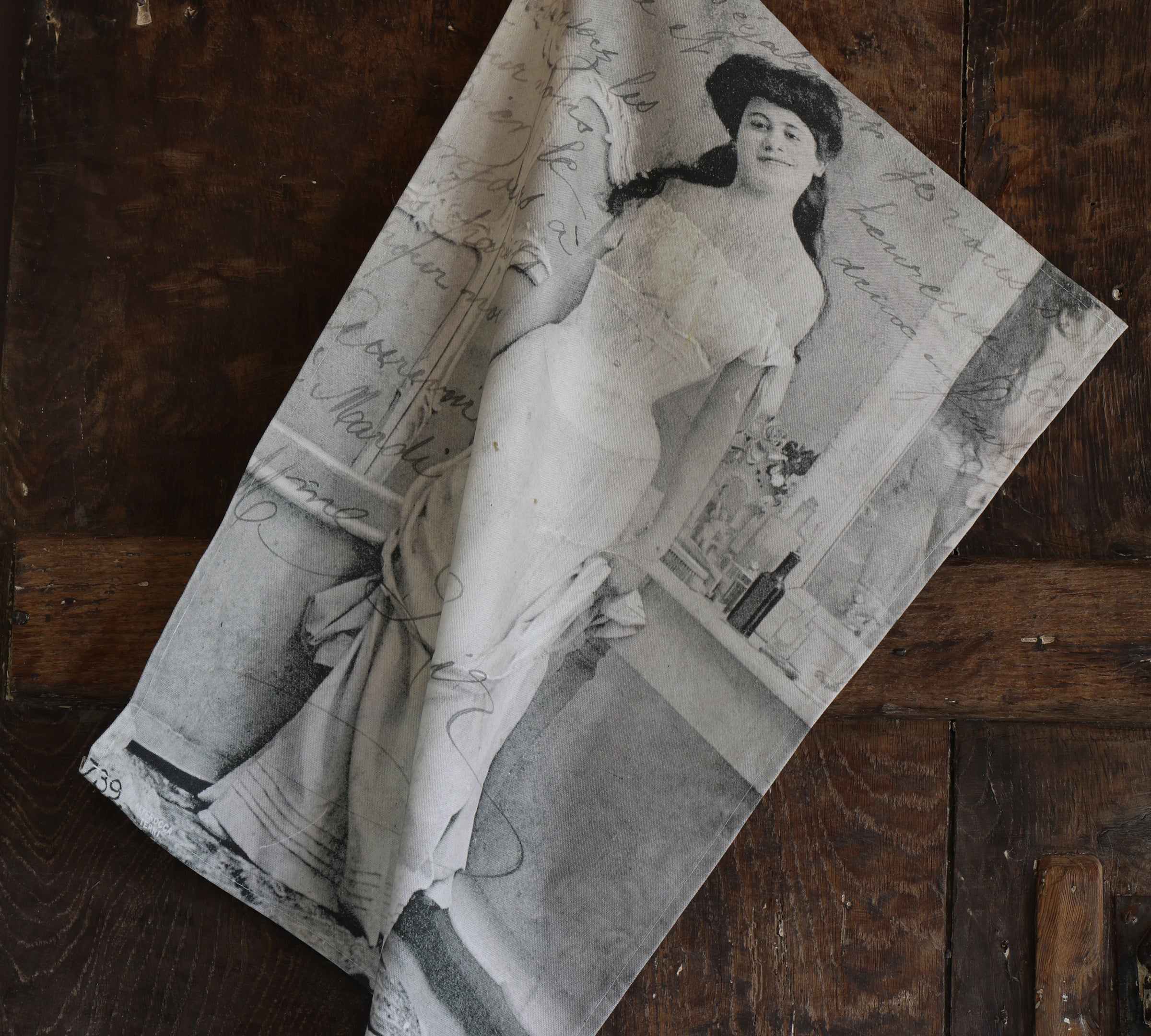 Tea towel featuring a black and white vintage postcard of a smiling lady in period dress hanging next to an old wooden door