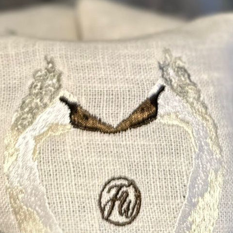 Close-up of textured Irish linen lavender pouch featuring a embroidered design of two swans touching beak to beak and the FW monogram