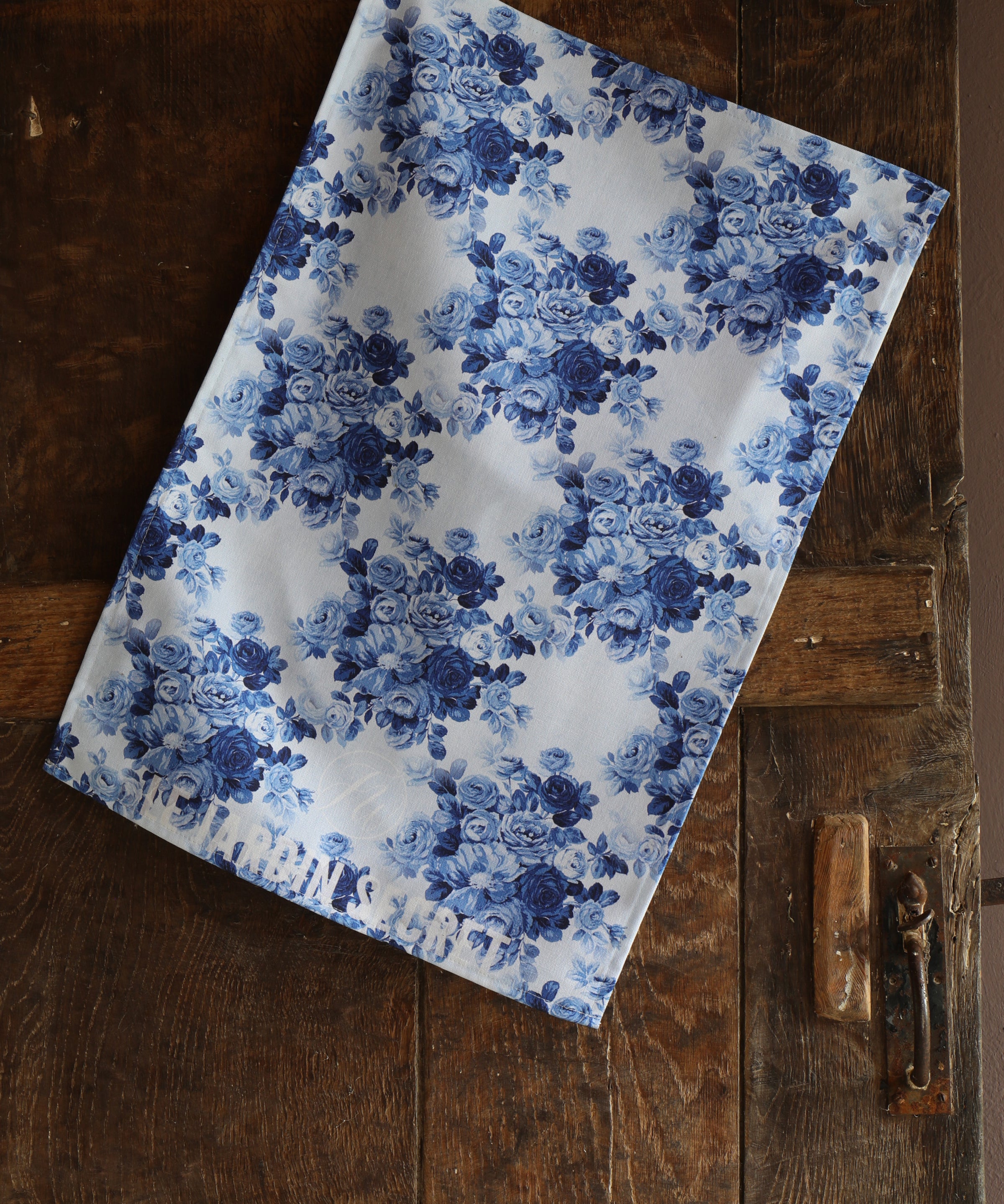 Blue floral patterned tea towel on a wooden surface with the words "Le Jardin Secret" at the bottom.