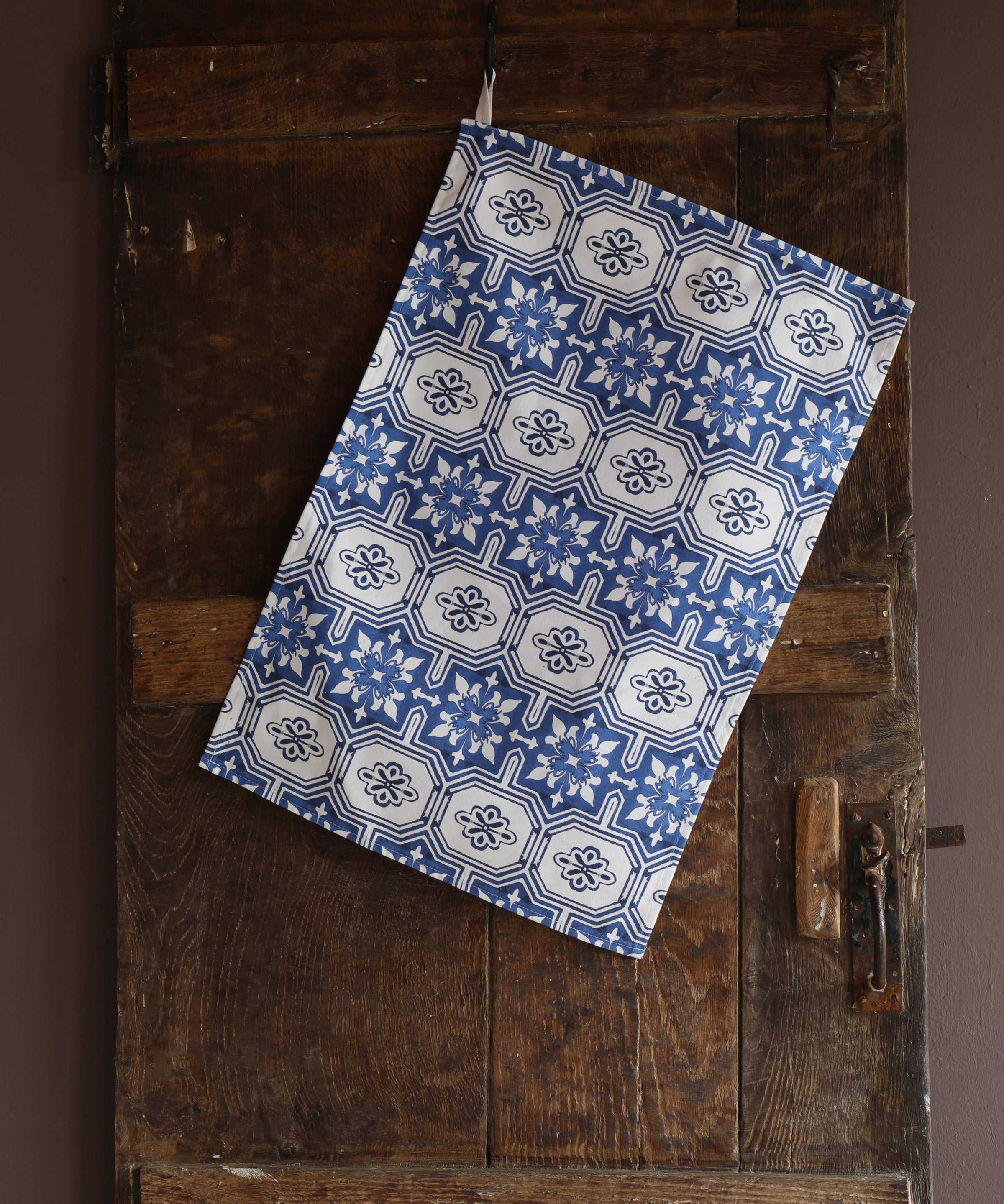 Tea towel with a repeating blue and white tiled pattern hanging on a wooden door
