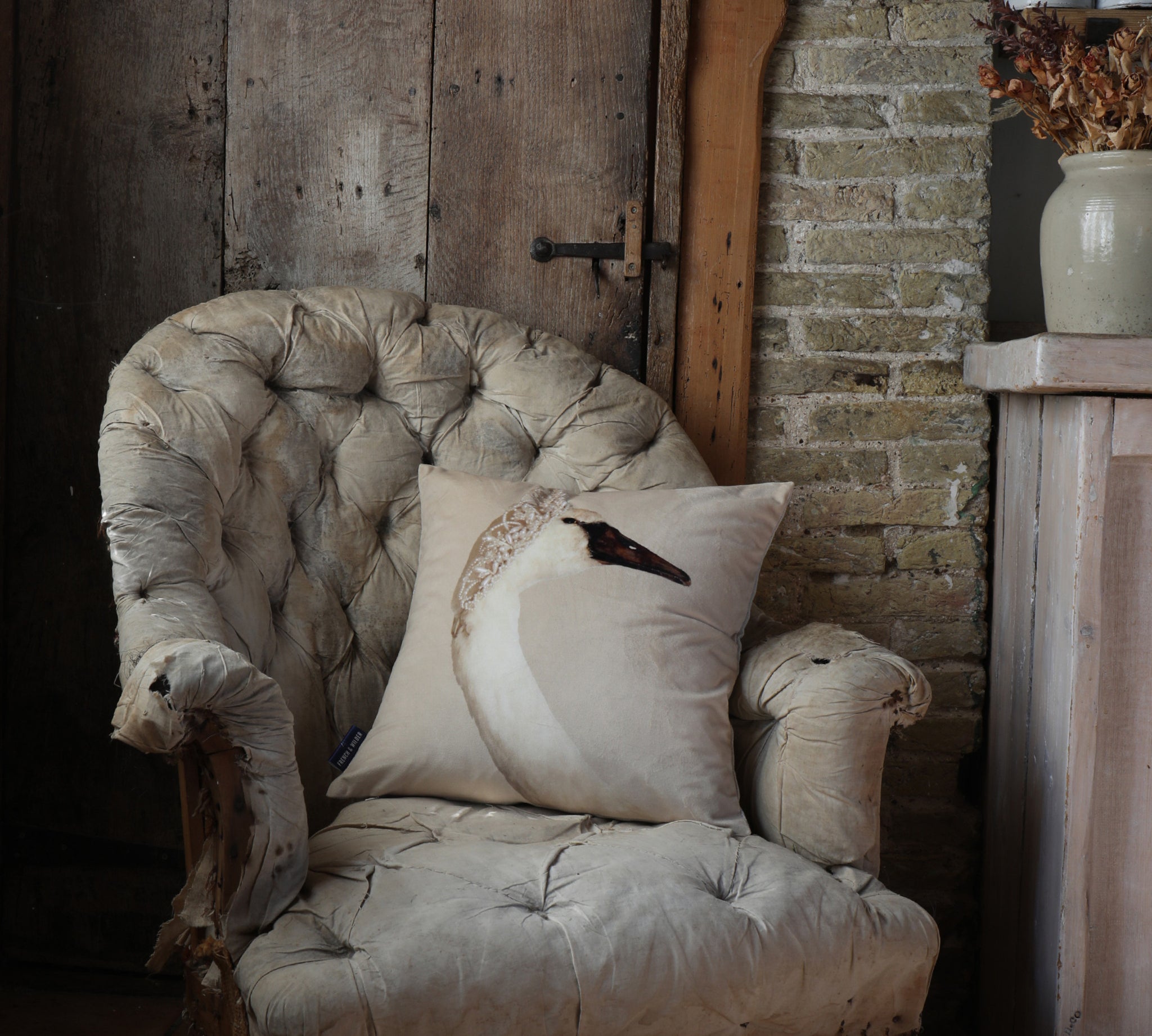 Decorative velvet cushion with an image of an elegant swan wearing a pearl tiara, sitting on a vintage armchair in a rustic setting.