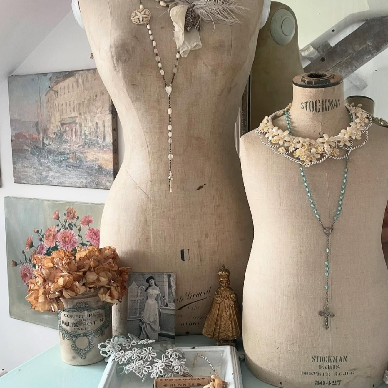 Two mannequin torsos with necklaces on a table with decorative items.