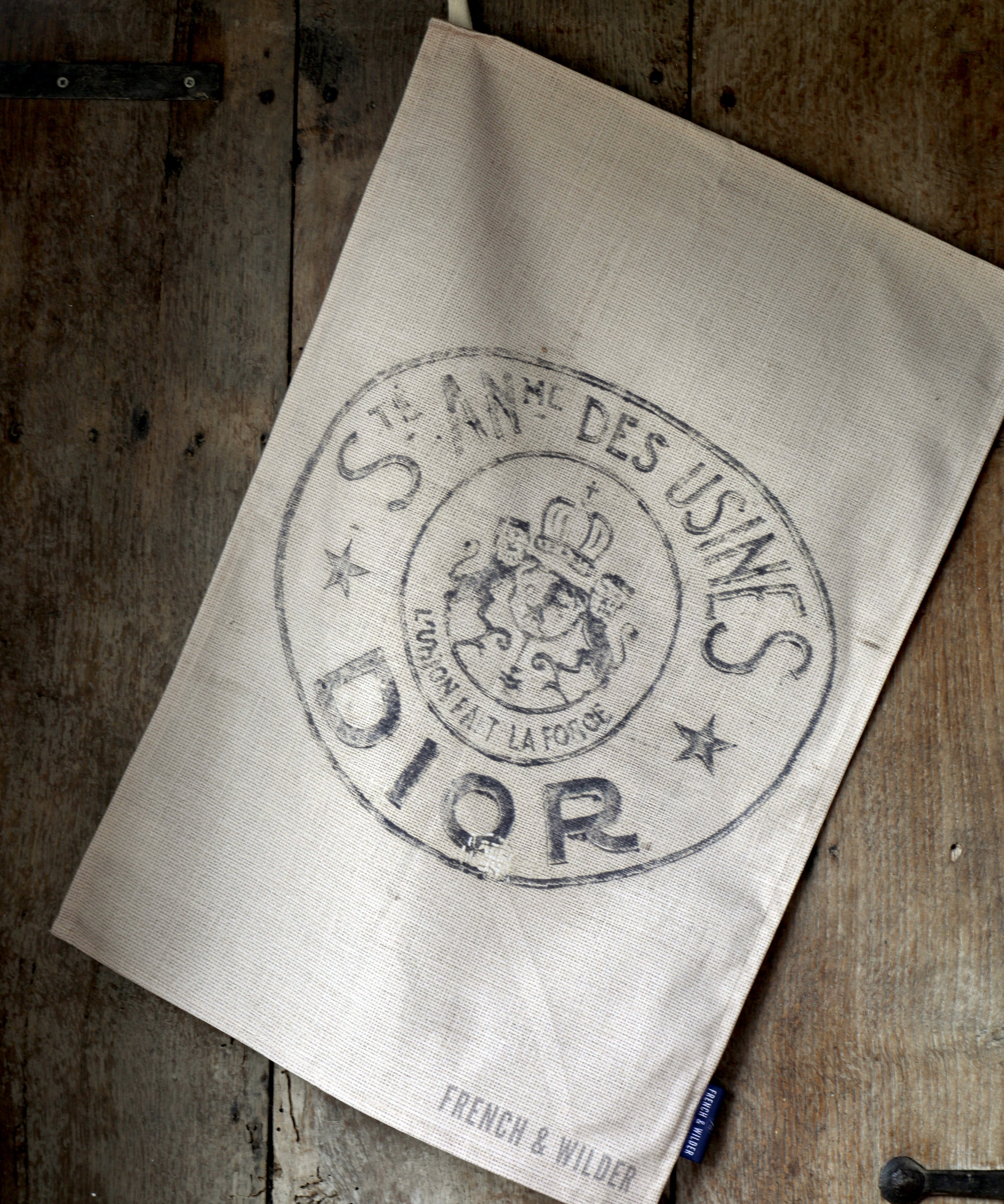 Tea towel with design featuring an old branded hessian bag, hanging against an old wooden door