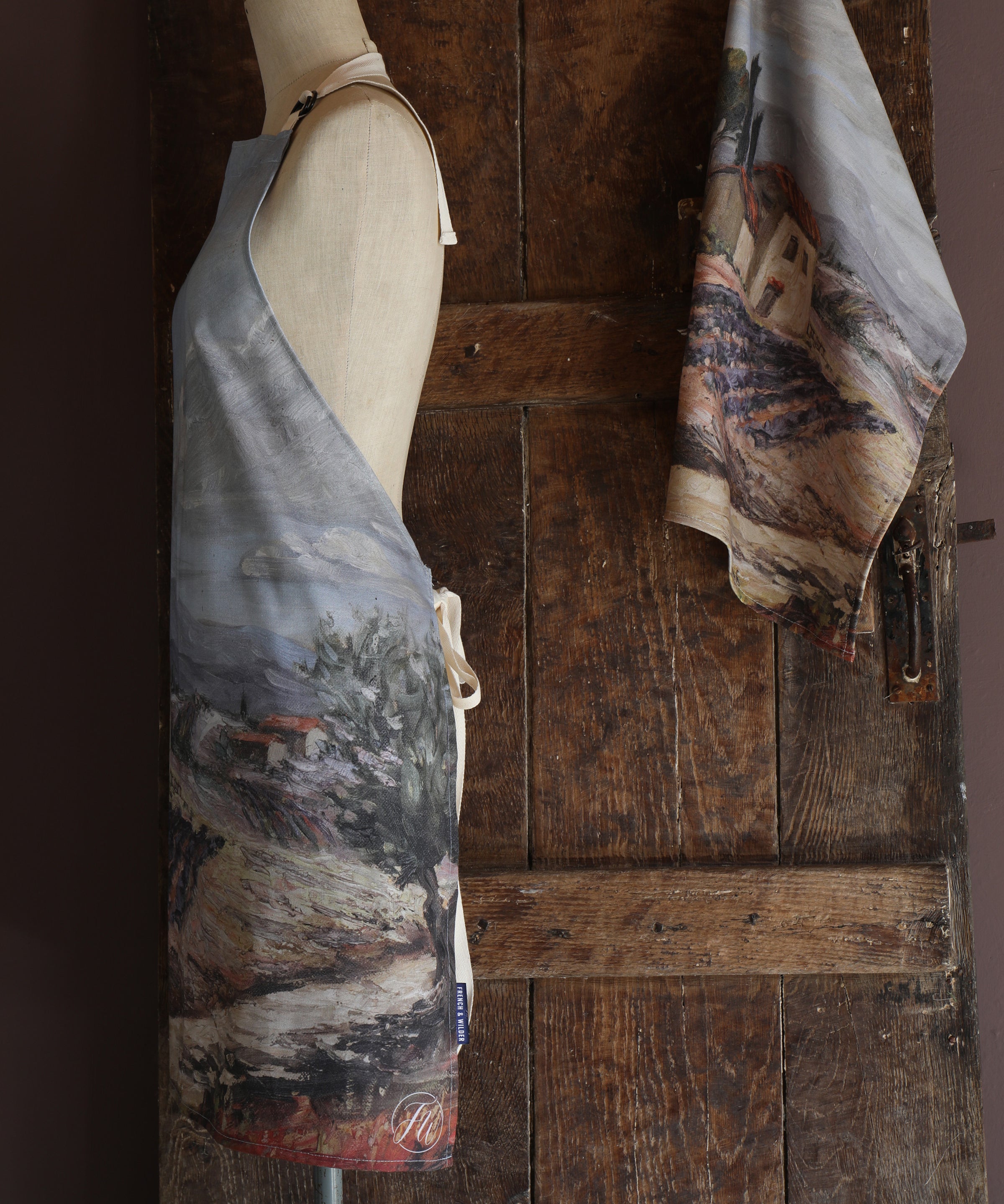 Mannequin wearing an apron with a design of a rural Provence design against a wooden background