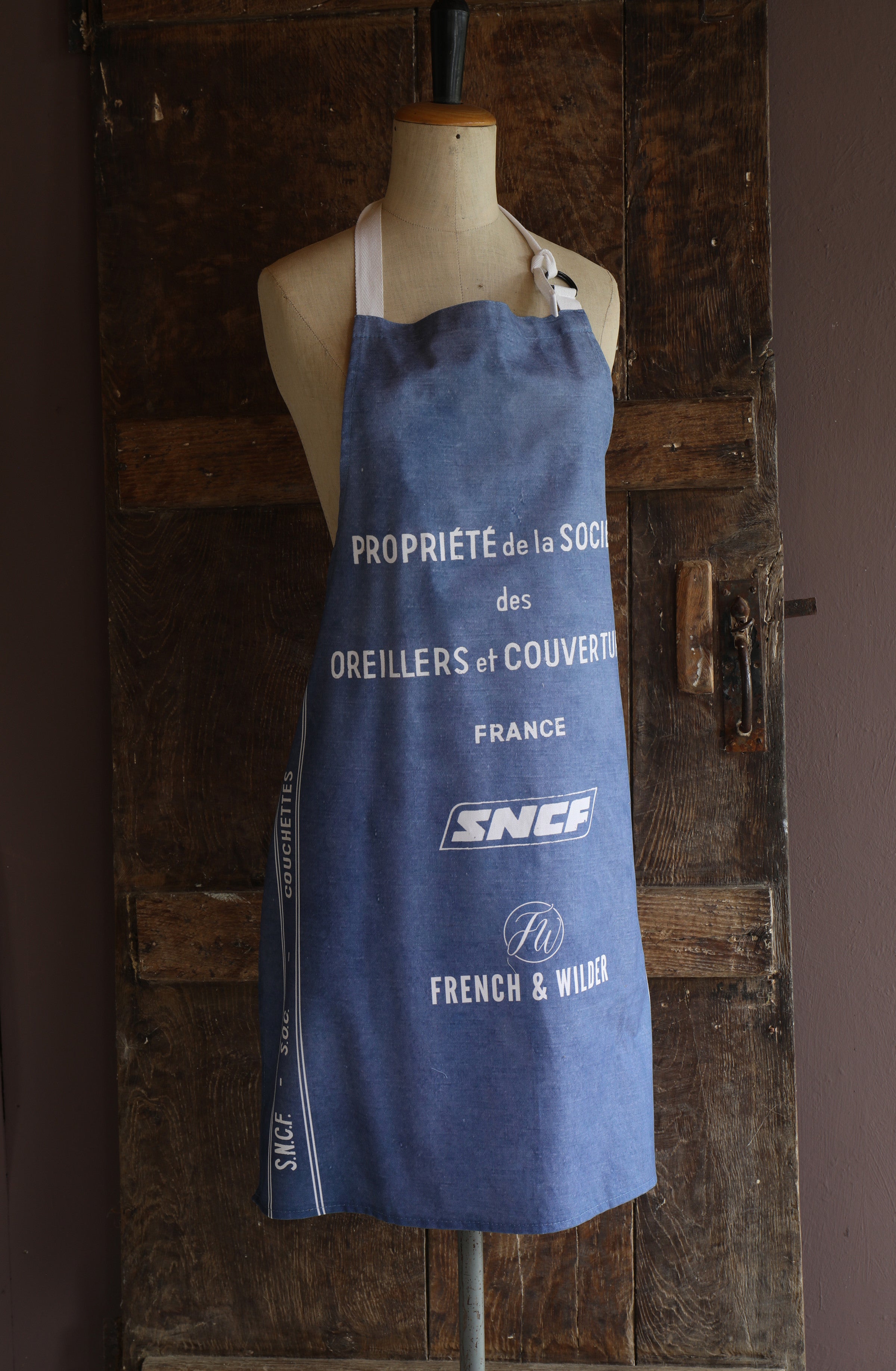 Apron with blue and white text and SNCF logo on a mannequin against a wooden background