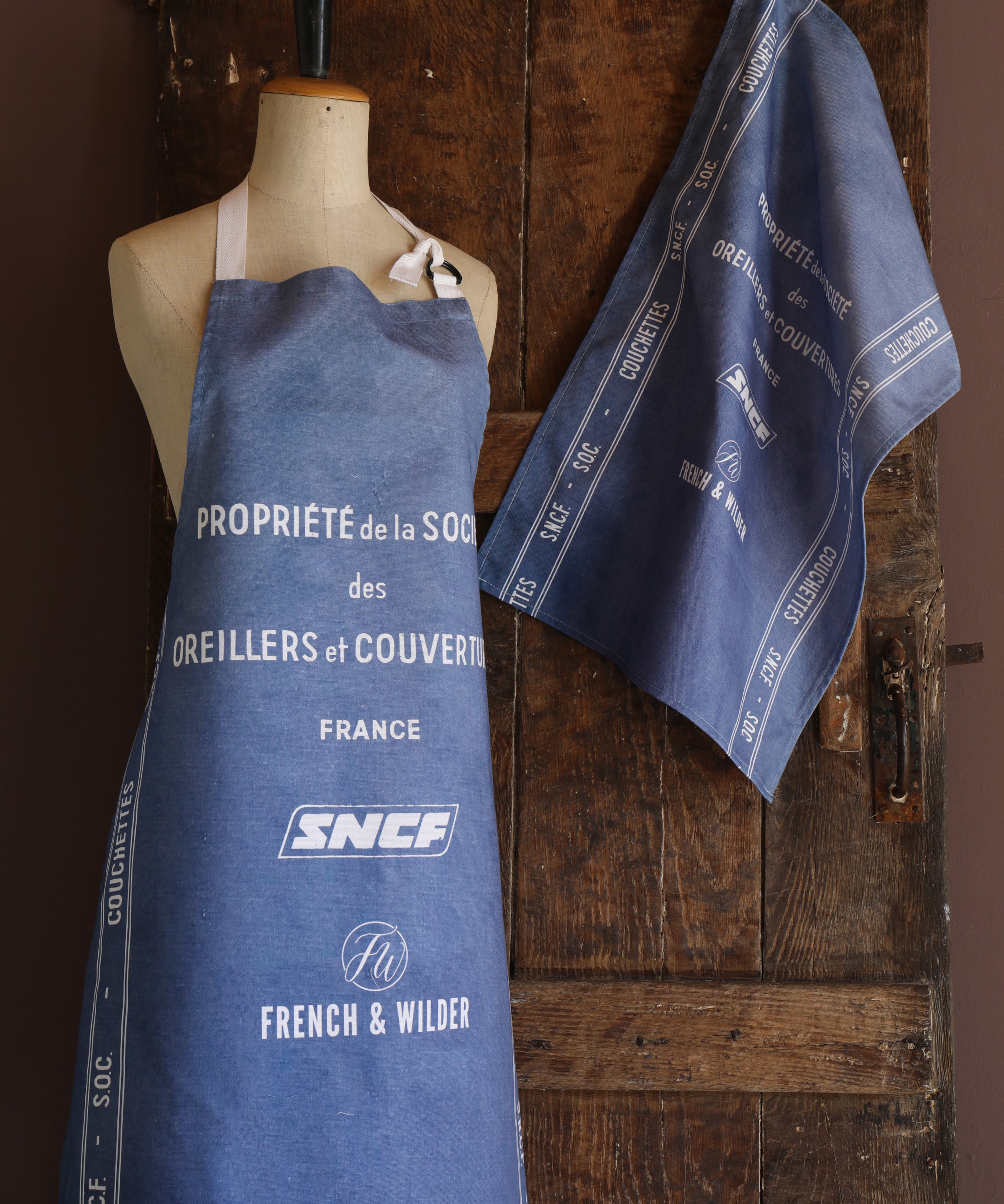 Mannequin wearing an apron with a blue and white SNCF design against a wooden background