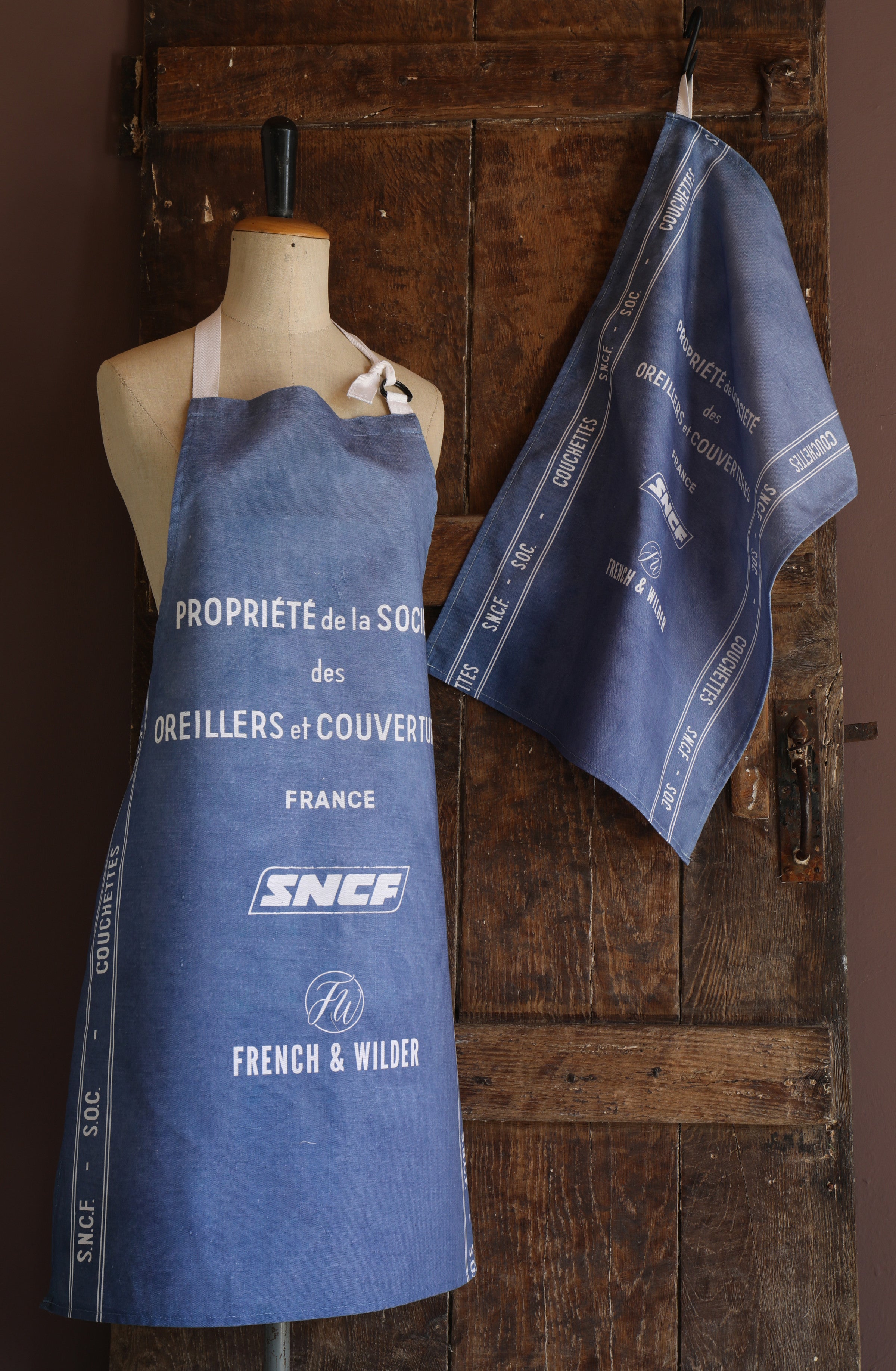 Mannequin wearing an apron with a blue and white SNCF design against a wooden background