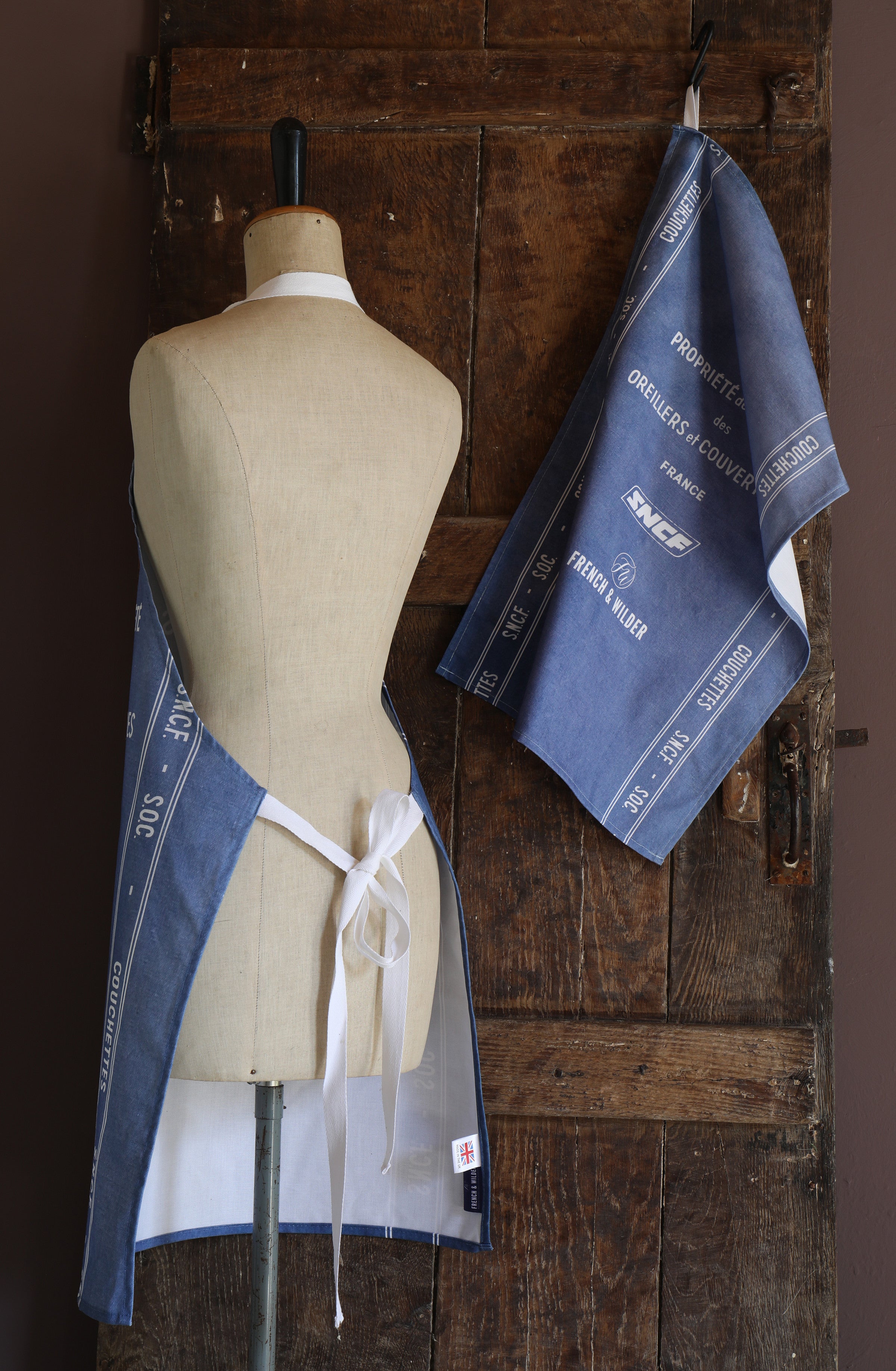 Mannequin wearing an apron with a blue and white SNCF design against a wooden background