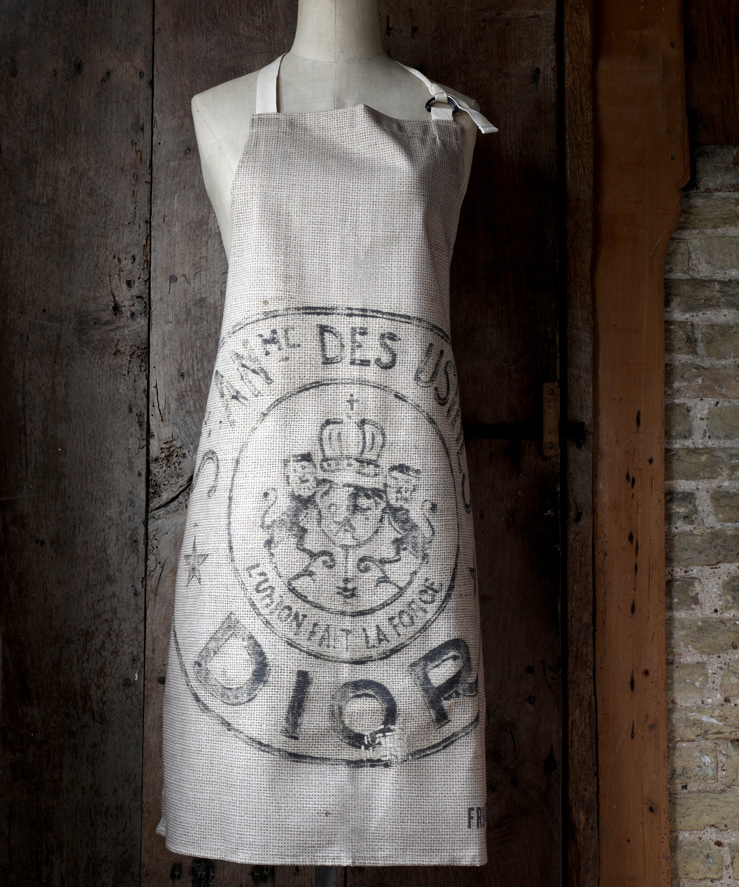Vintage-style apron with a logo on a mannequin against a rustic wooden door