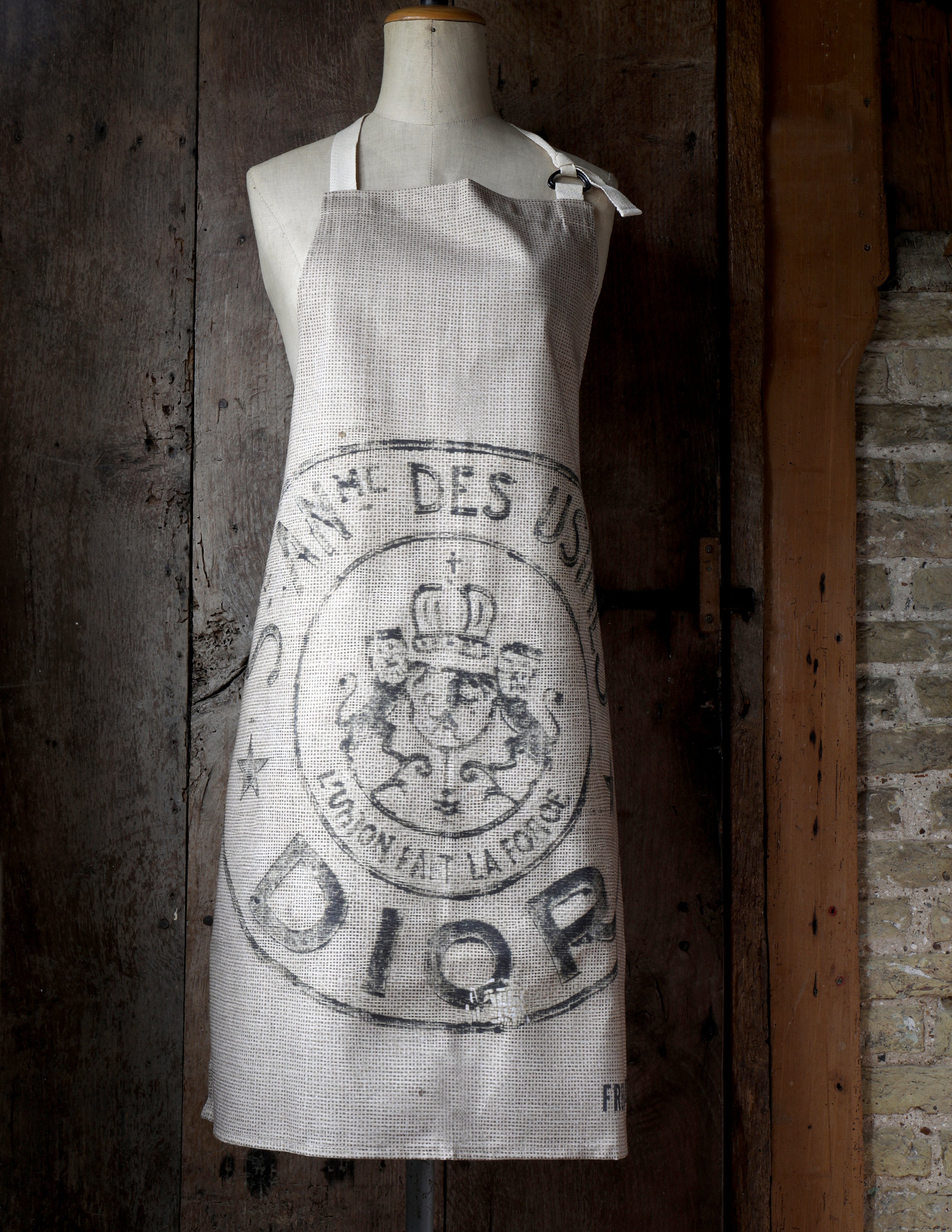Vintage-style apron with a logo on a mannequin against a rustic wooden door