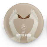 Decorative button badge with two swans forming a heart shape and 'French & Wilder' branding.