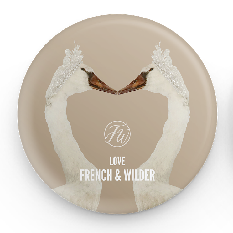 Decorative button badge with two swans forming a heart shape and 'French & Wilder' branding.