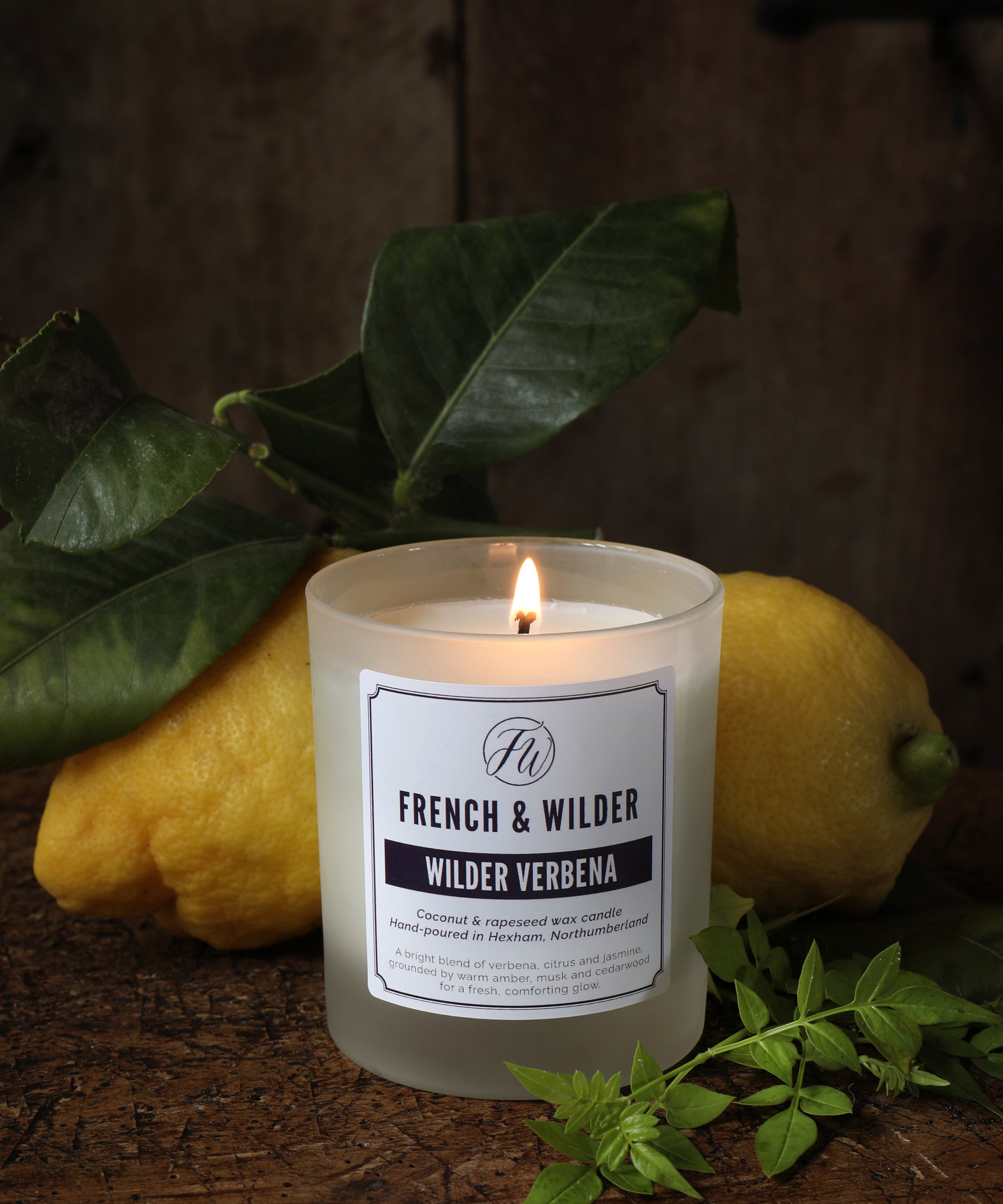 Candle in a frosted glass container on a wooden surface with lemons and leaves