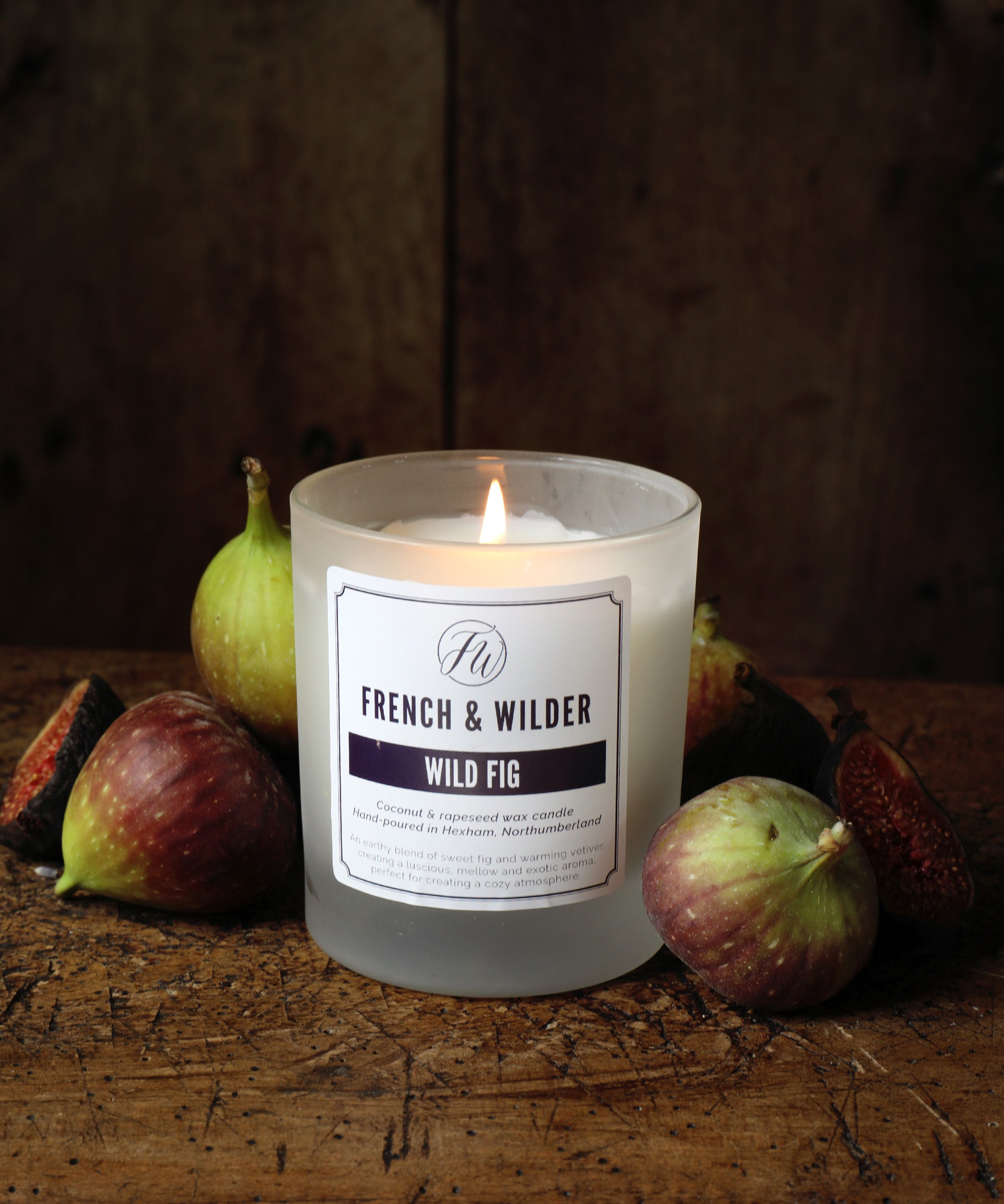 Candle in a frosted glass container surrounded by figs on a wooden surface