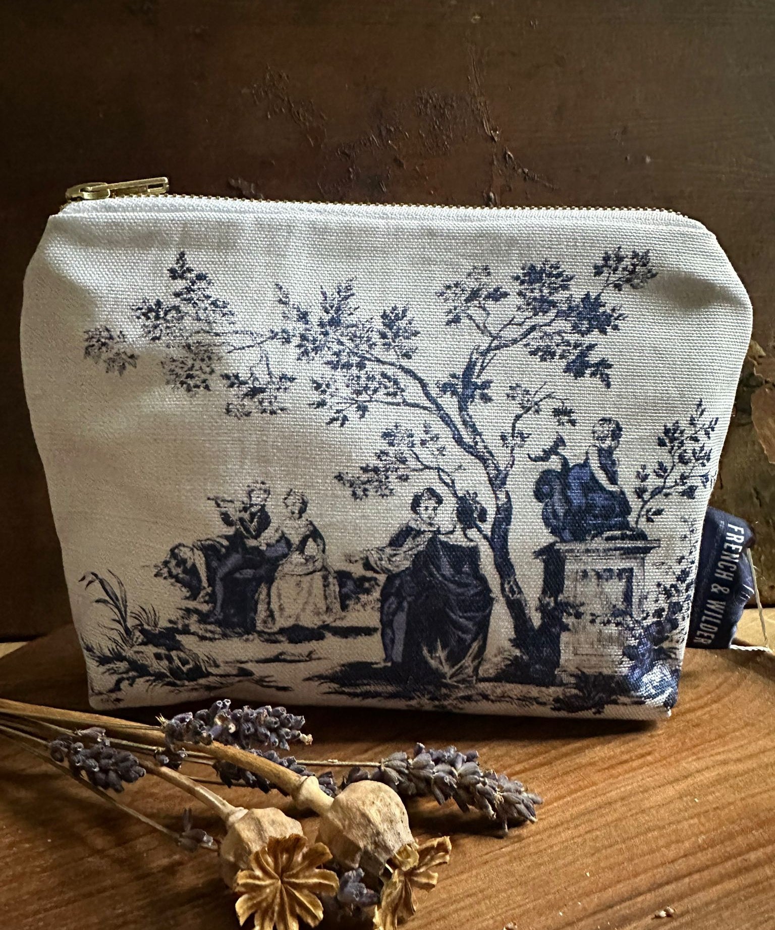 Fabric pouch with vintage toile de jouy design on a wooden surface with dried flowers.