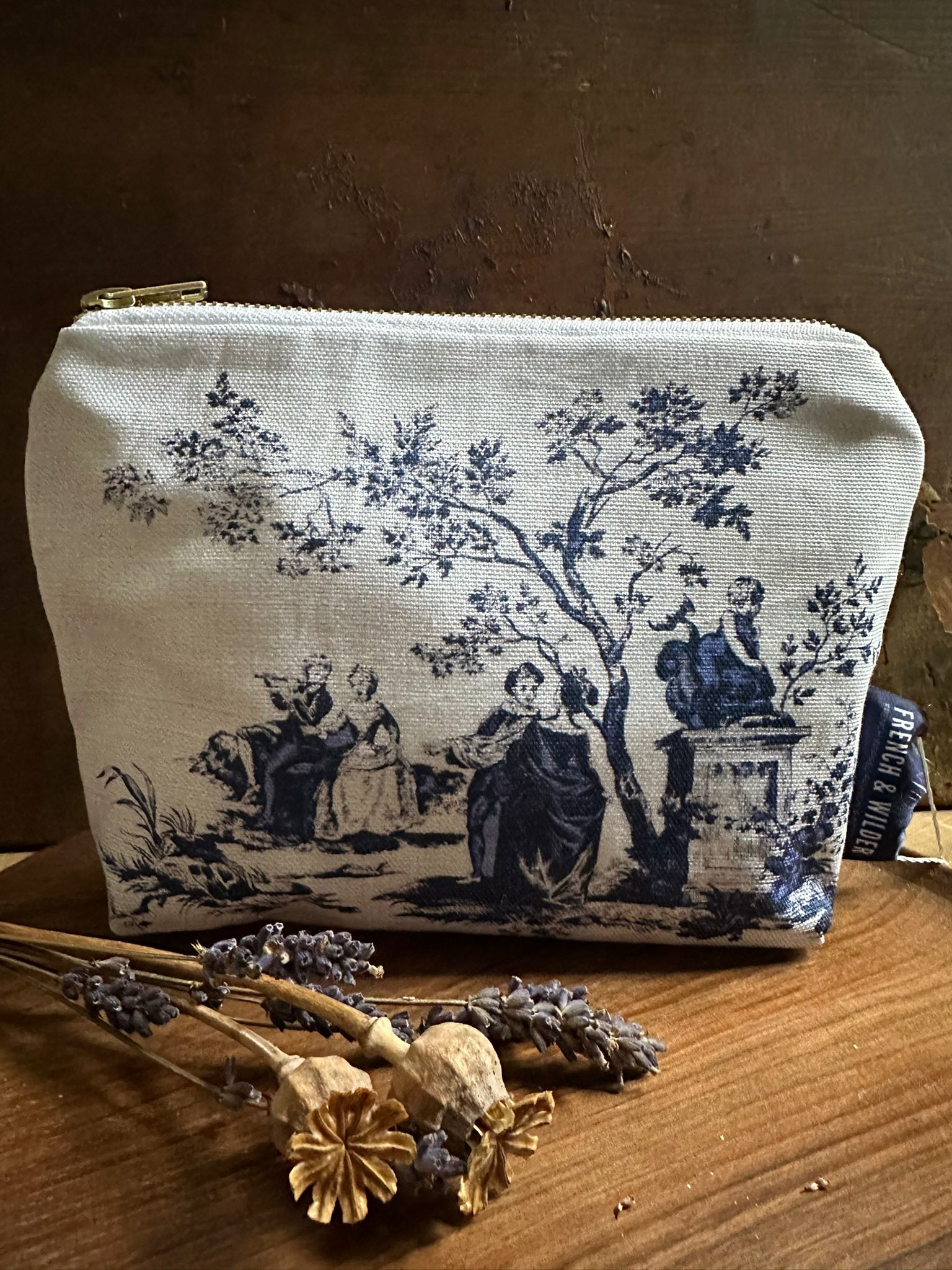 Fabric pouch with vintage toile de jouy design on a wooden surface with dried flowers.