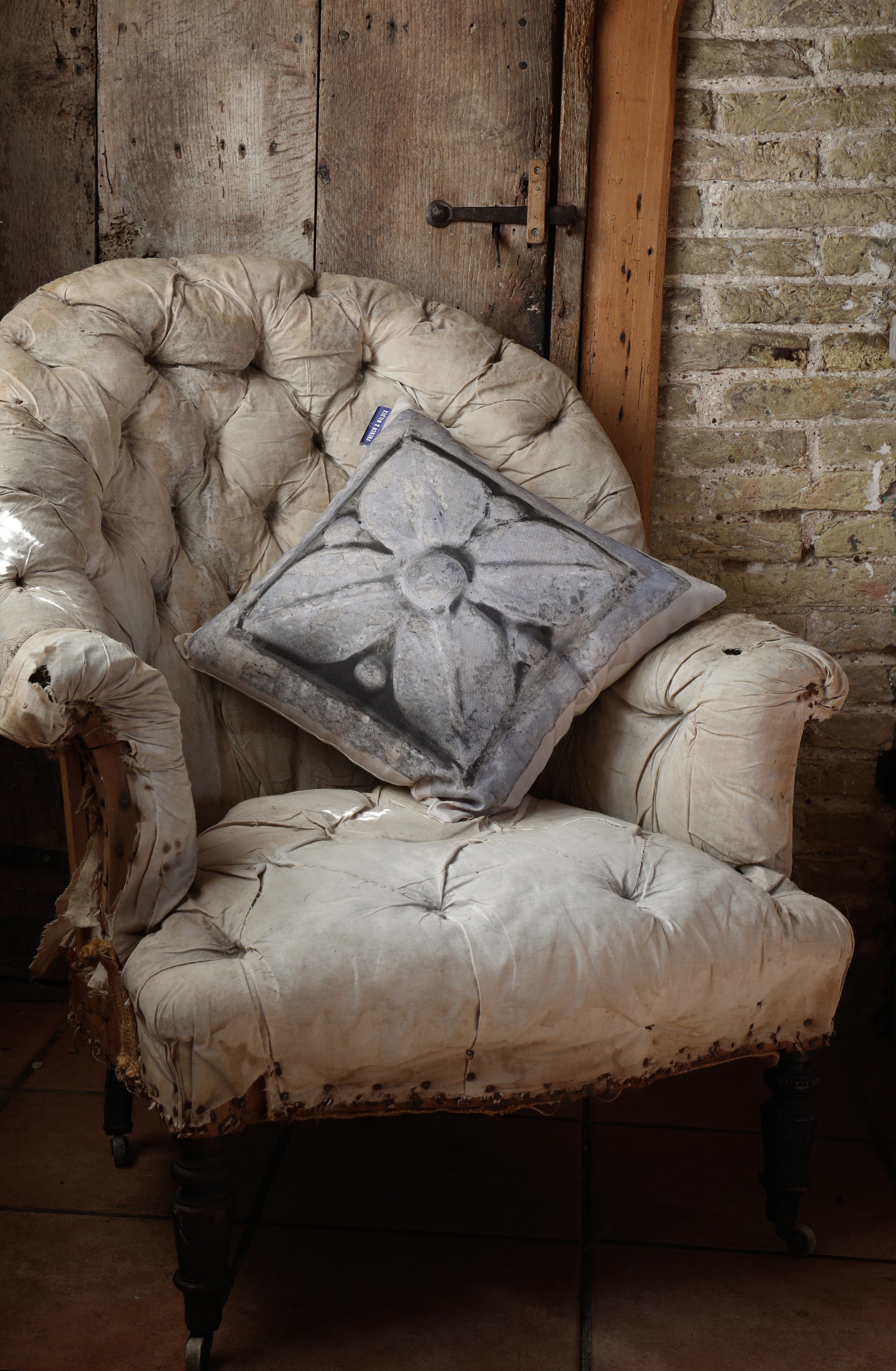 A cushion with an image of a textured stone decoration on a vintage armchair against a rustic brick wall.