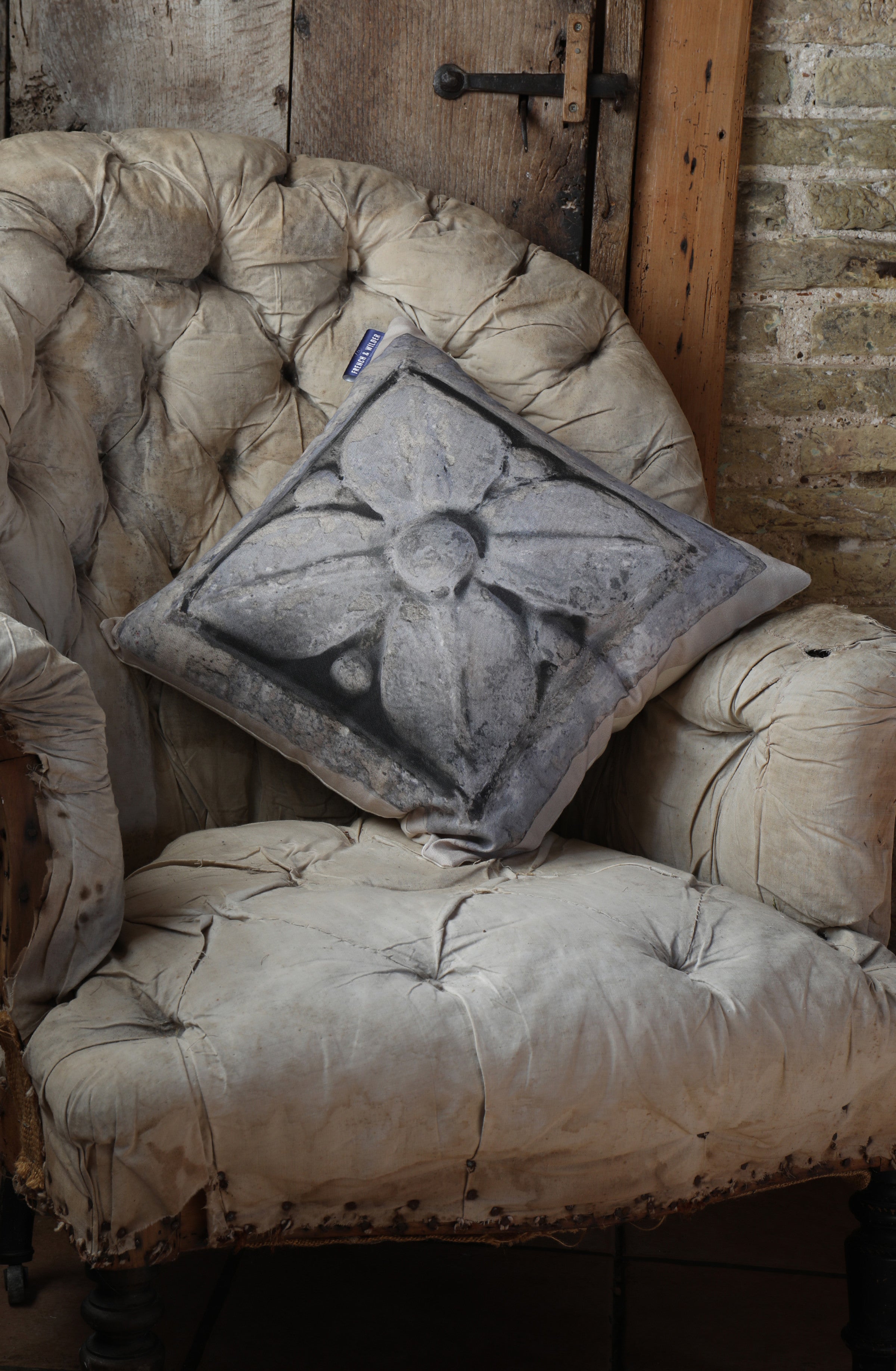 Decorative pillow with a decorative ornamental stone design placed carefully on an old armchair against a rustic brick wall and wooden door