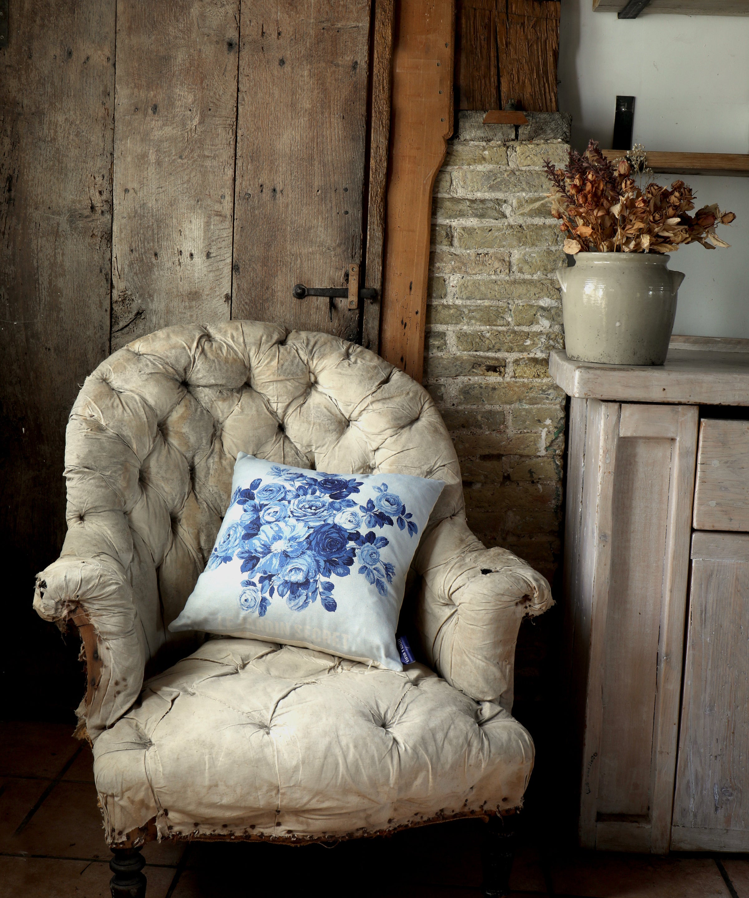 Blue floral design pillow sitting on a vintage armchair in a rustic room.