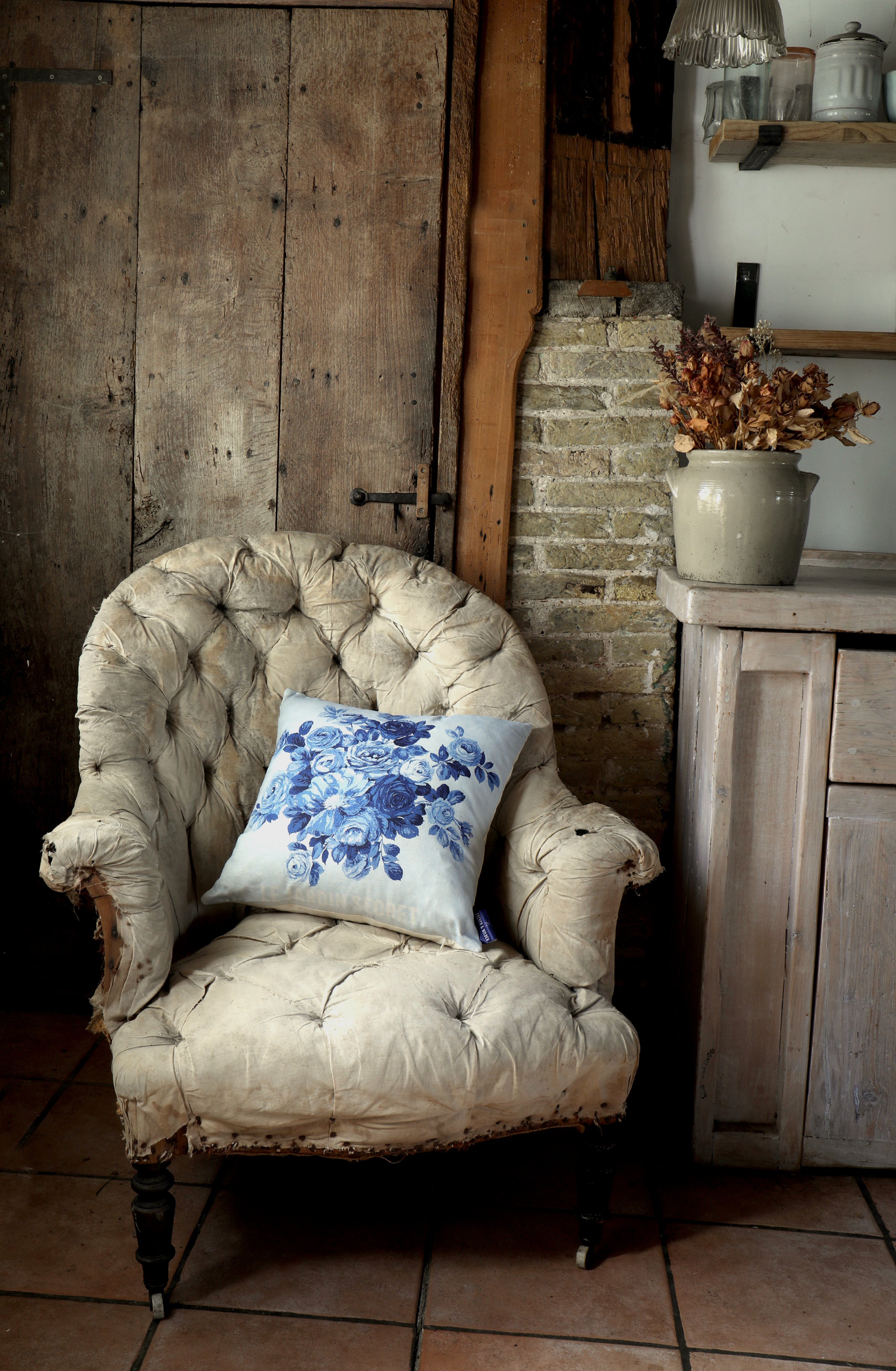 Blue floral design pillow sitting on a vintage armchair in a rustic room.