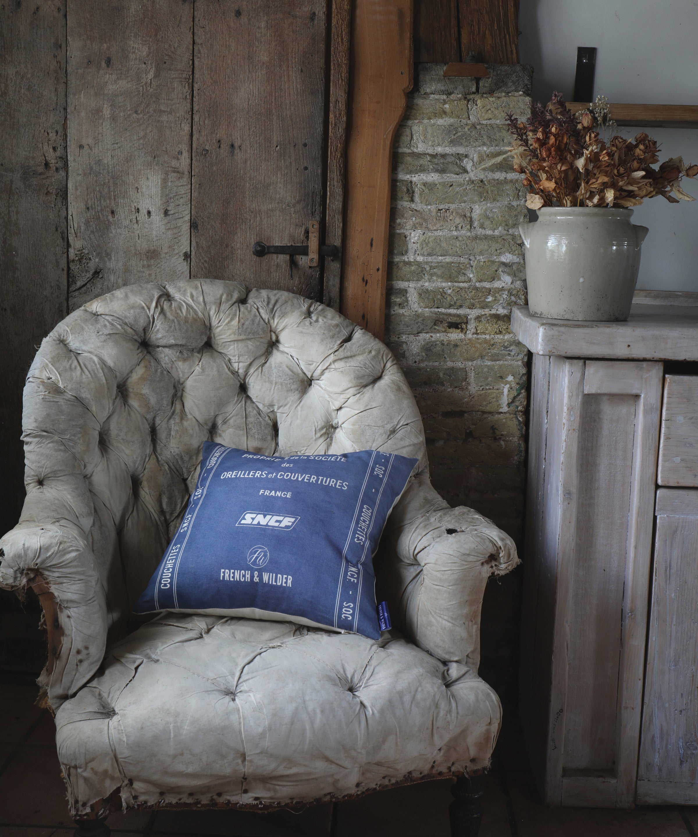 Blue cushion with white SNCF branding placed on a vintage armchair in a rustic room.