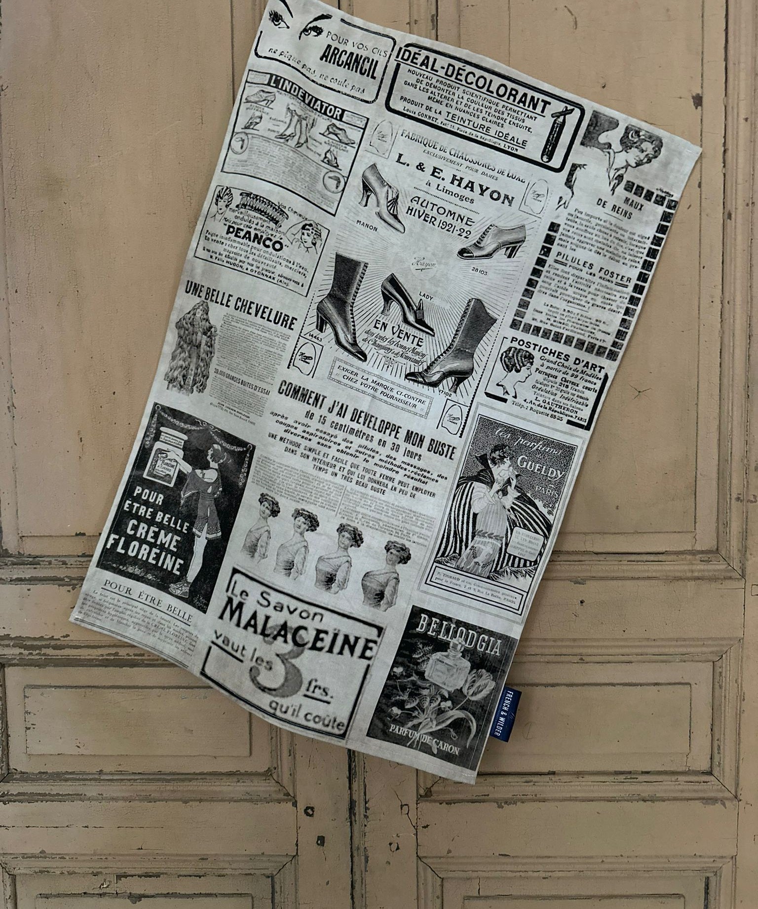 Tea towel with a design of vintage French beauty and fashion advertisements hanging next to a painted wooden door