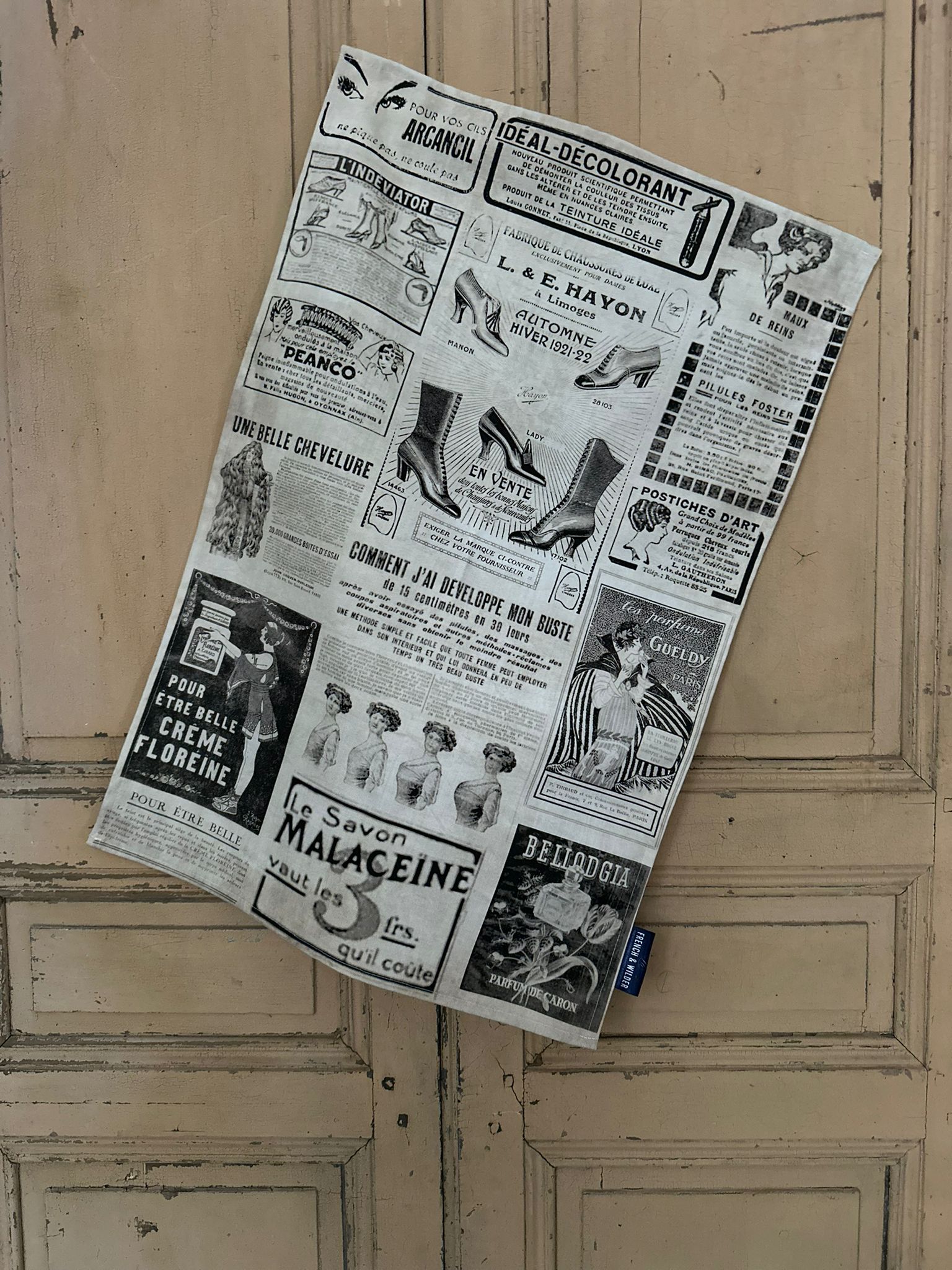 Tea towel with a design of vintage French beauty and fashion advertisements hanging next to a painted wooden door