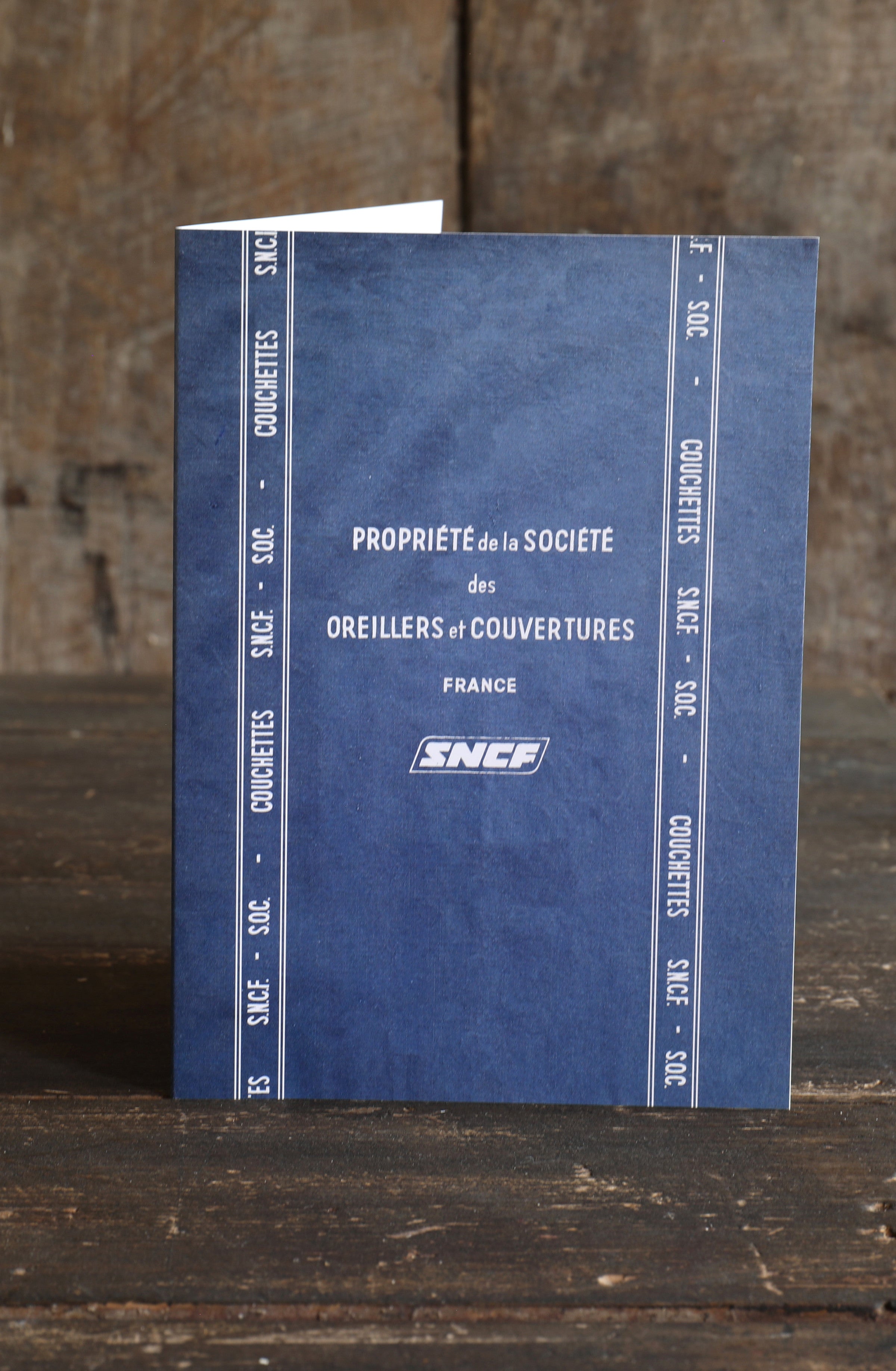 Blue greetings card with white text SNCF branding on a wooden surface