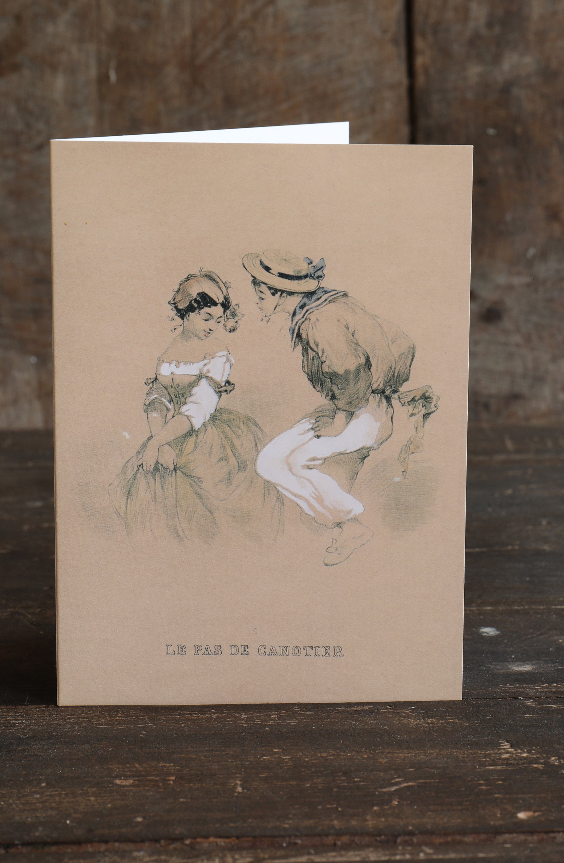 Greetings card with a vintage line-drawn illustration of two young people with the words 'Le Pas de Canotier' on a rustic wooden background