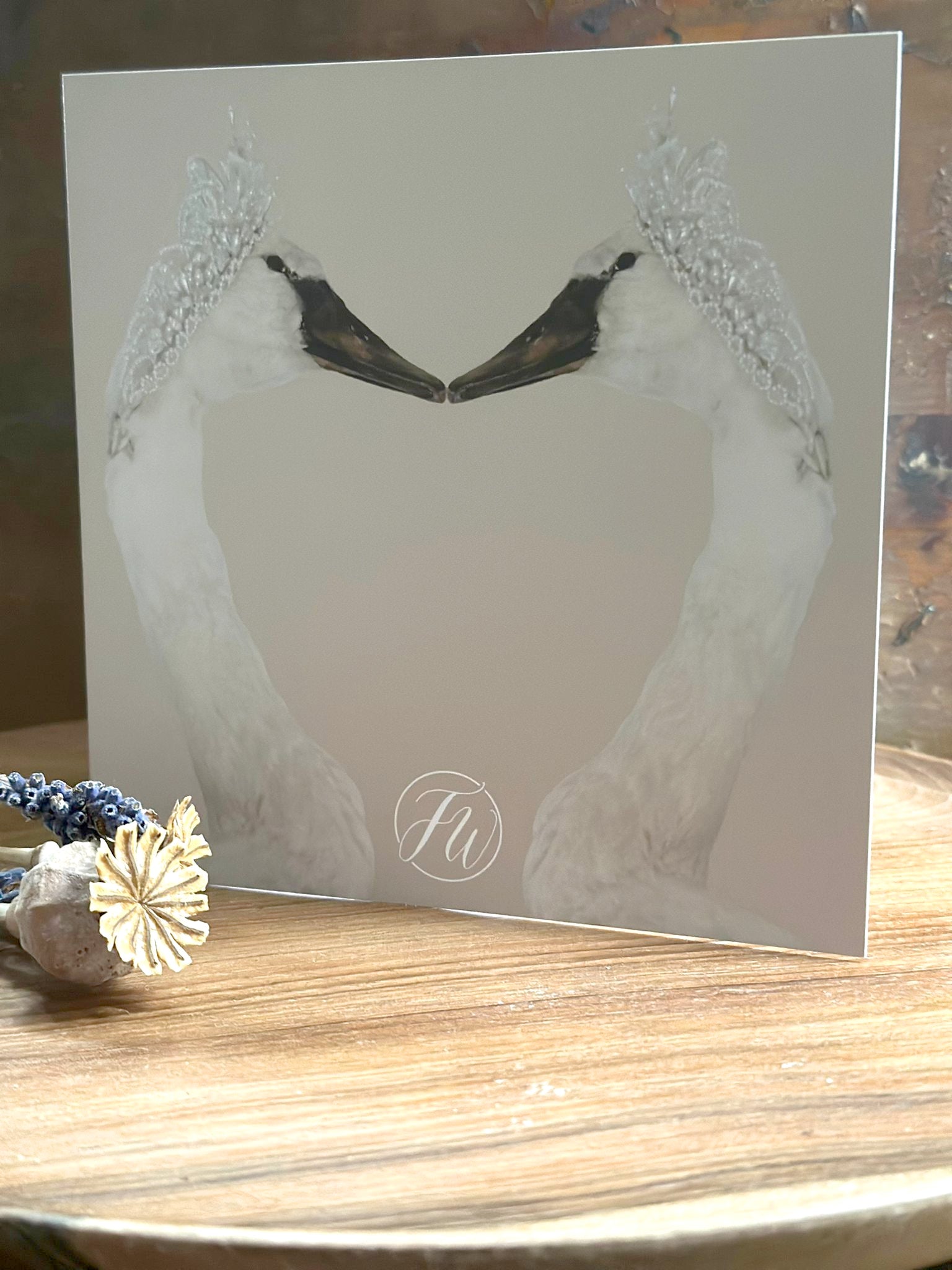 Greetings card featuring a design of two swans touching beak to beak with the FW logo, placed on a wooden surface.