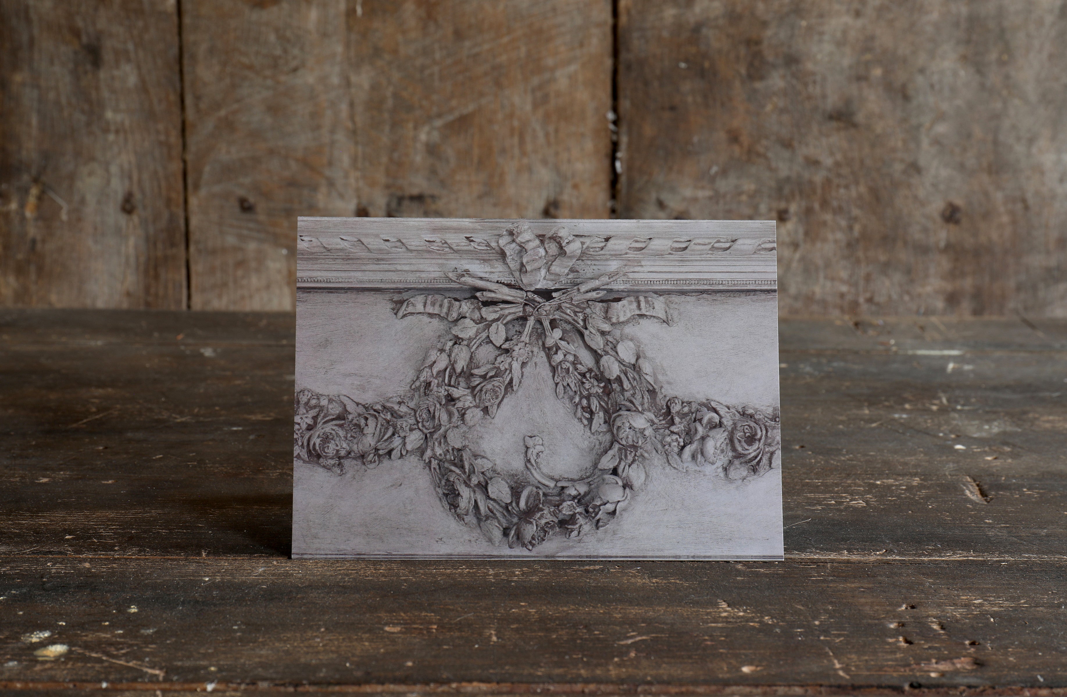 Decorative greetings card with design of a grey plaster moulding in a wreath design on a wooden surface