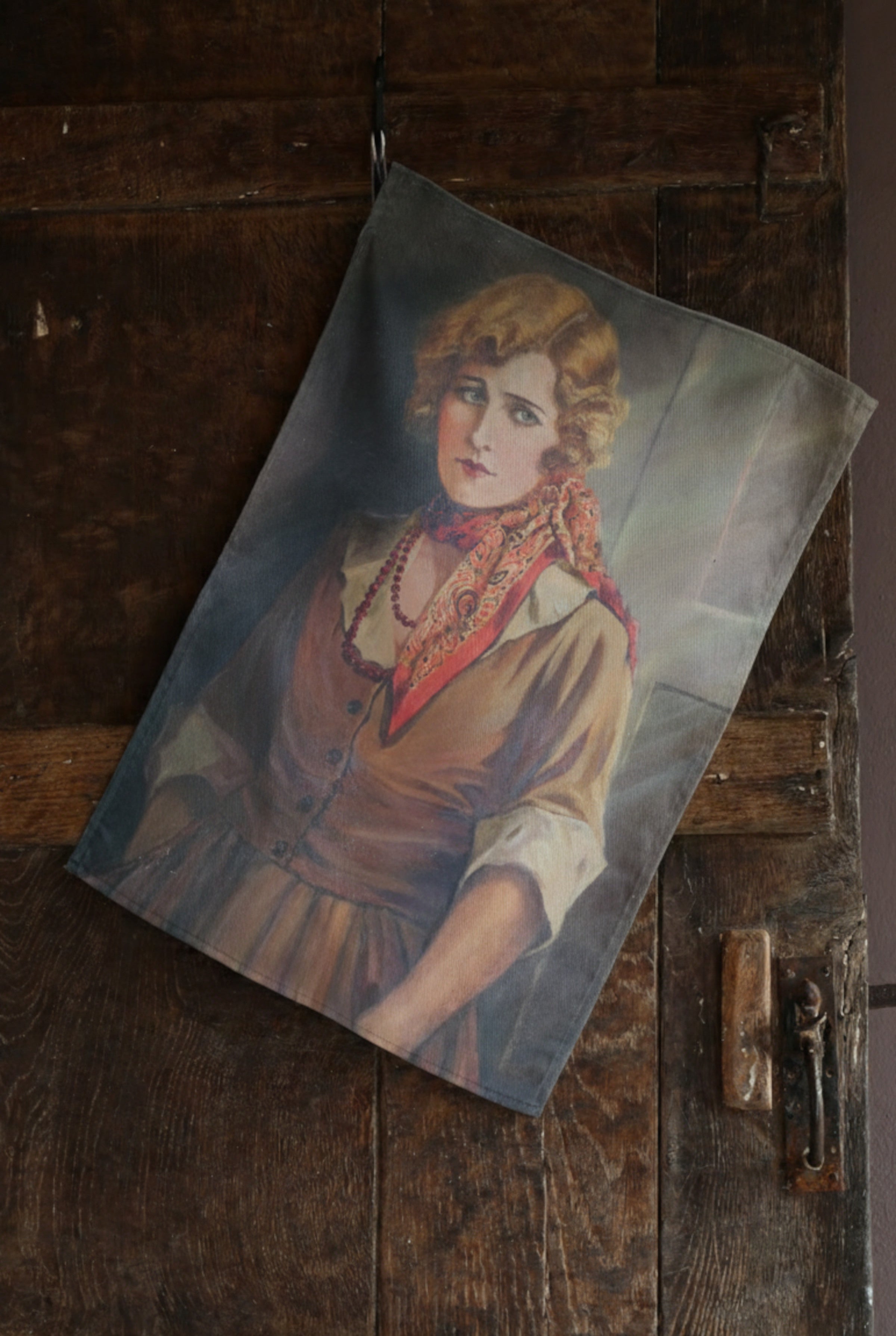 Tea towel featuring the vintage portrait of a woman with a serious gaze in elegant early 20th century fashion hanging from a dark wooden door