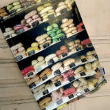 Tea towel featuring brightly colour selection of meringues in a French shop window hanging next to a light colour painted wooden door