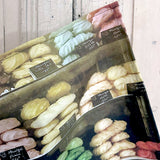 Detail of a tea towel featuring an image of meringues in a French shop window against a painted wooden surface.