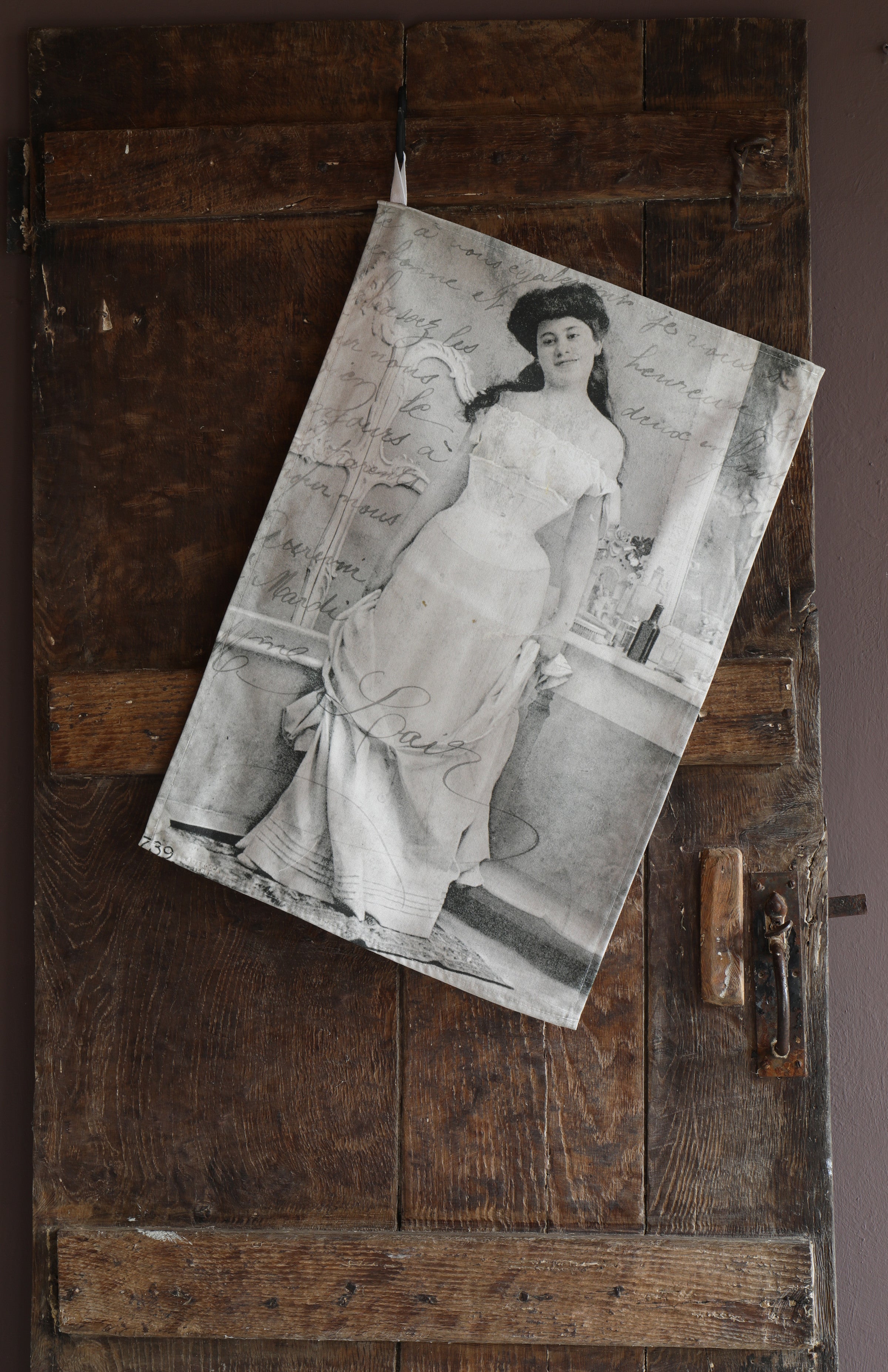 Tea towel hanging on an old wooden door with the image of a vintage postcard containing a black and white photograph of a smartly dressed woman