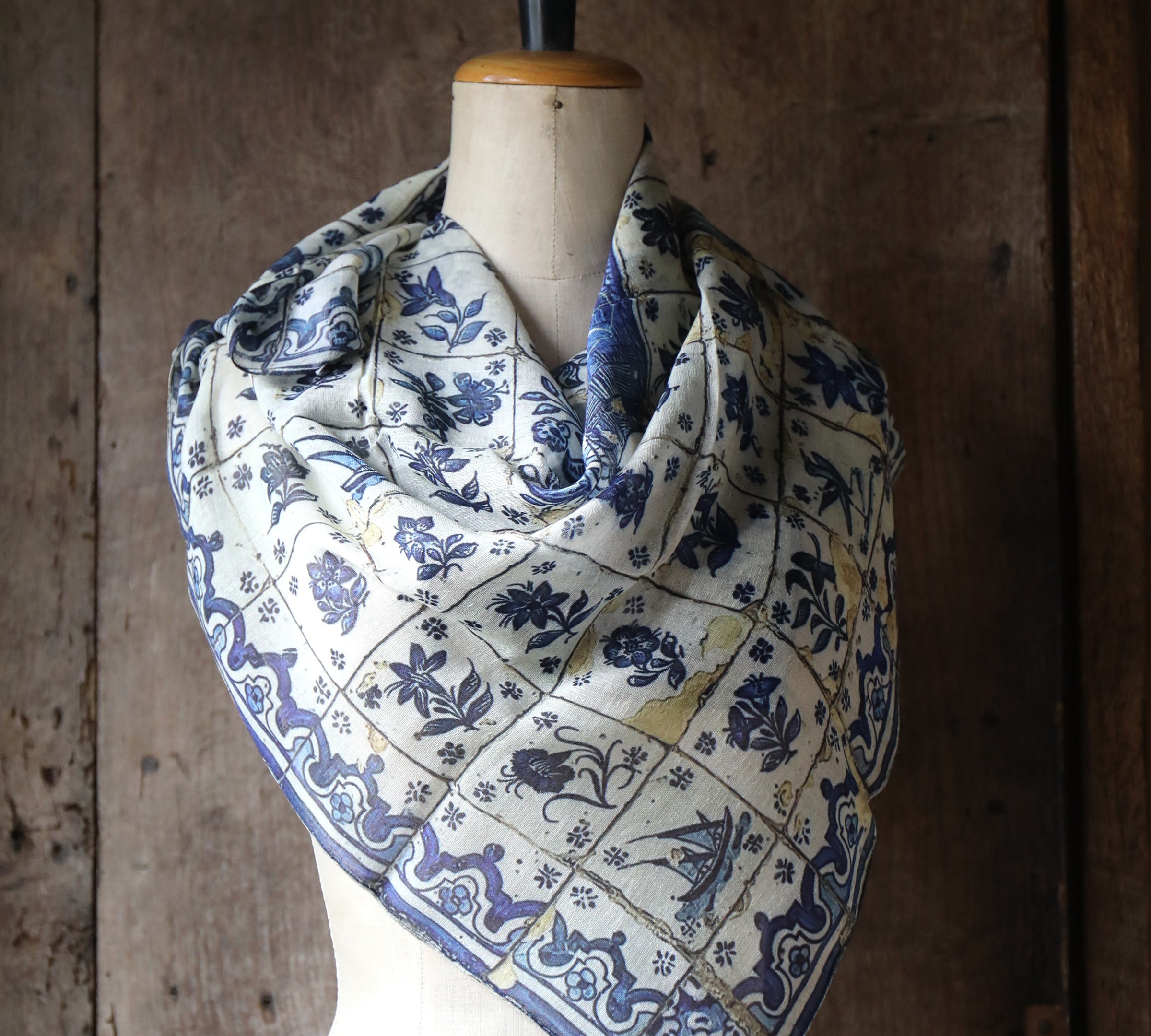 Mannequin wearing a blue and white tile pattern scarf against a wooden background