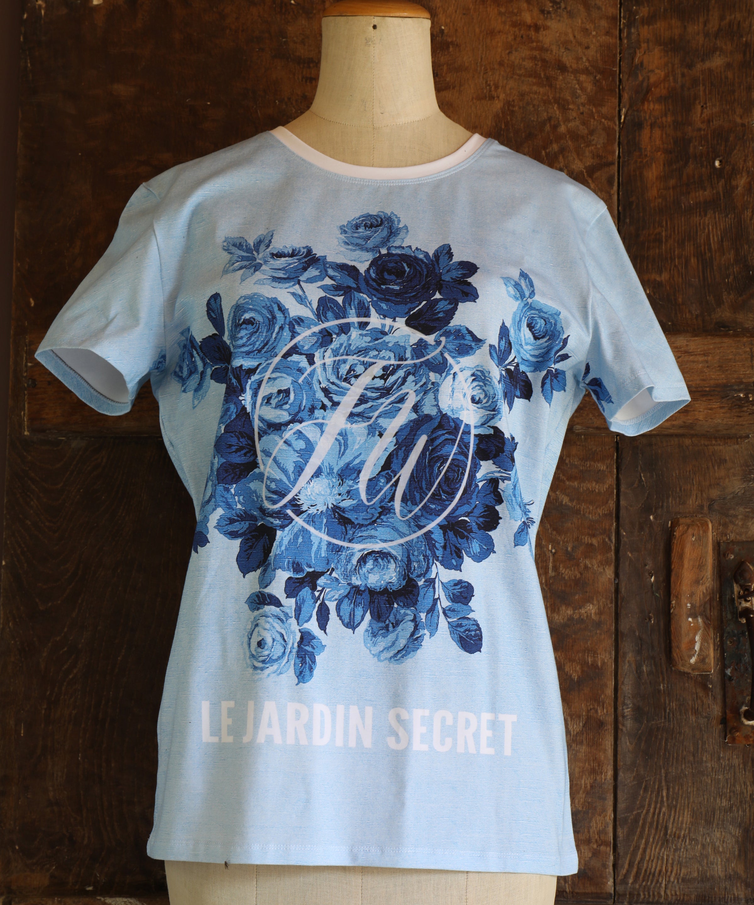 T-shirt with blue floral design and 'Le Jardin Secret' text on a mannequin against a wooden background