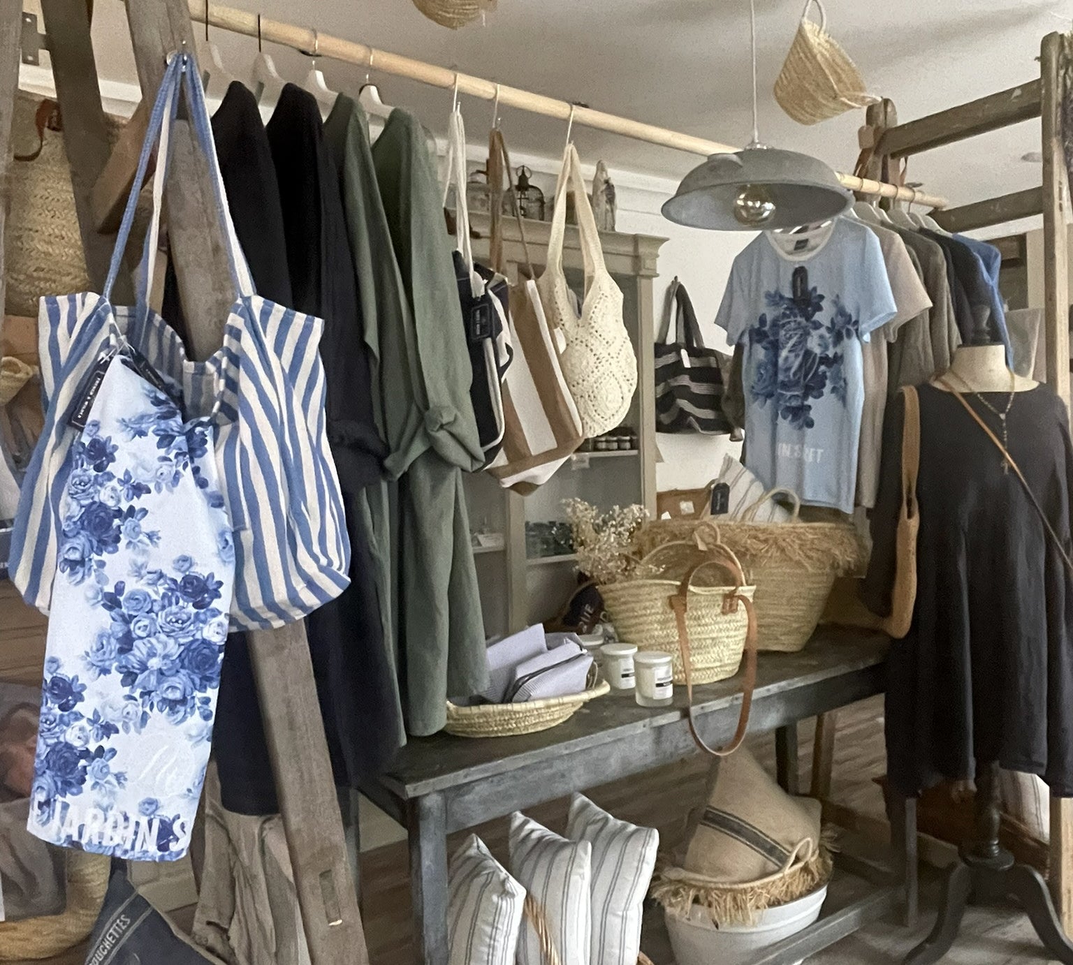 Homeware and clothing store interior with hanging clothes, cushions, bags, and baskets on a wooden rack.
