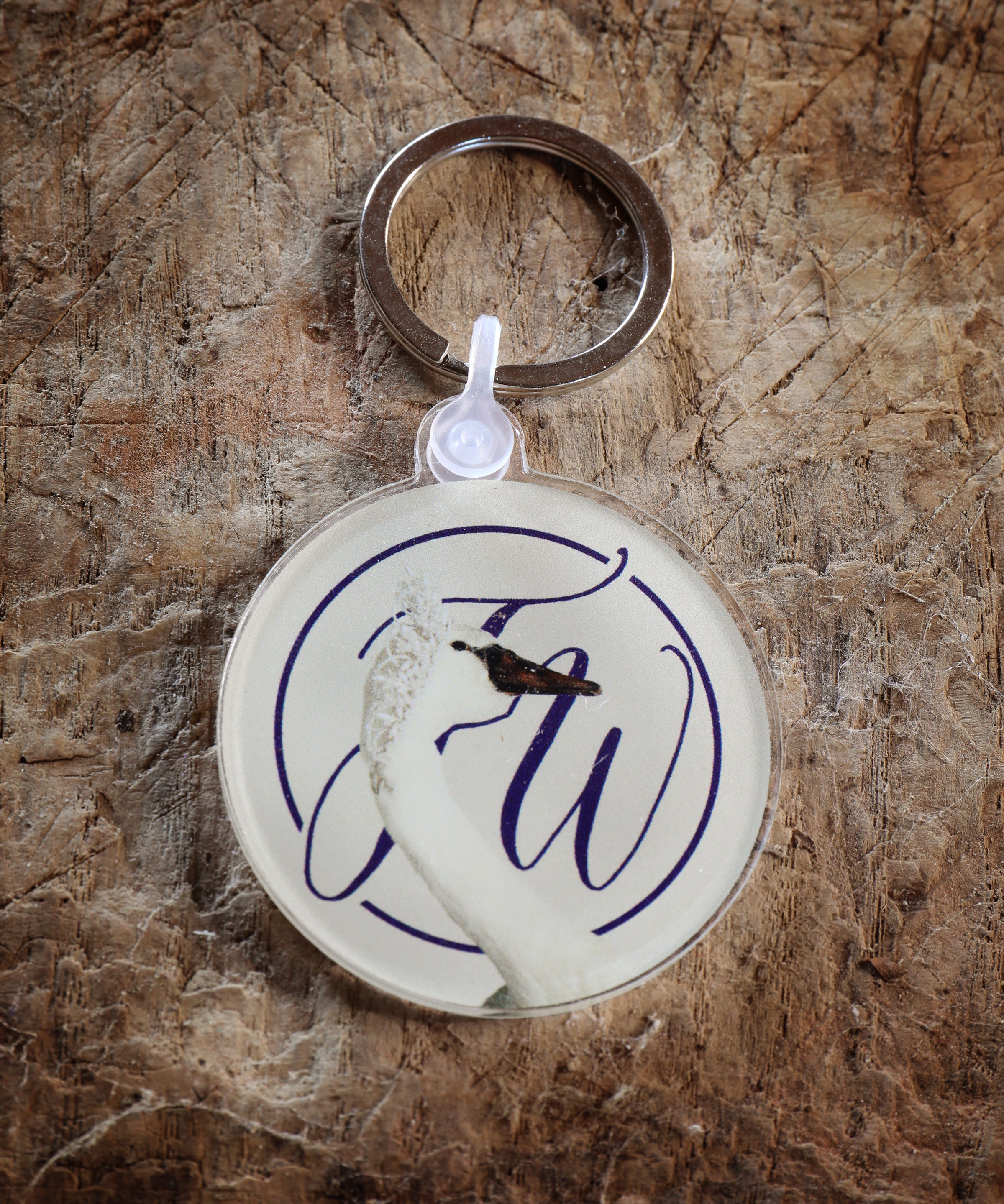 Keychain with circular design featuring a graceful swan and monogram photographed against a rough textured surface