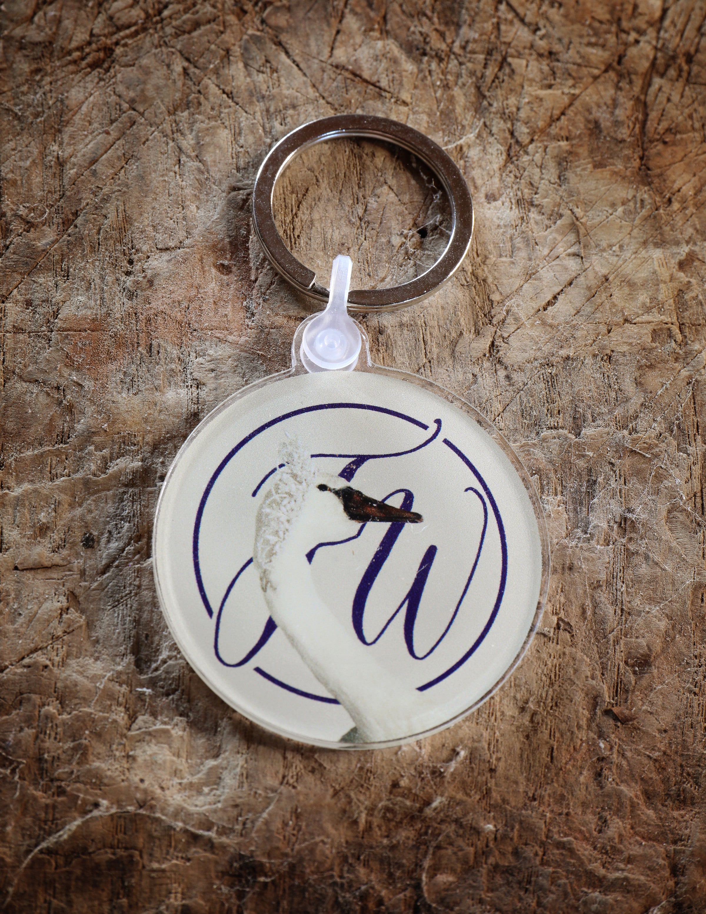 Keychain with circular design featuring a graceful swan and monogram photographed against a rough textured surface