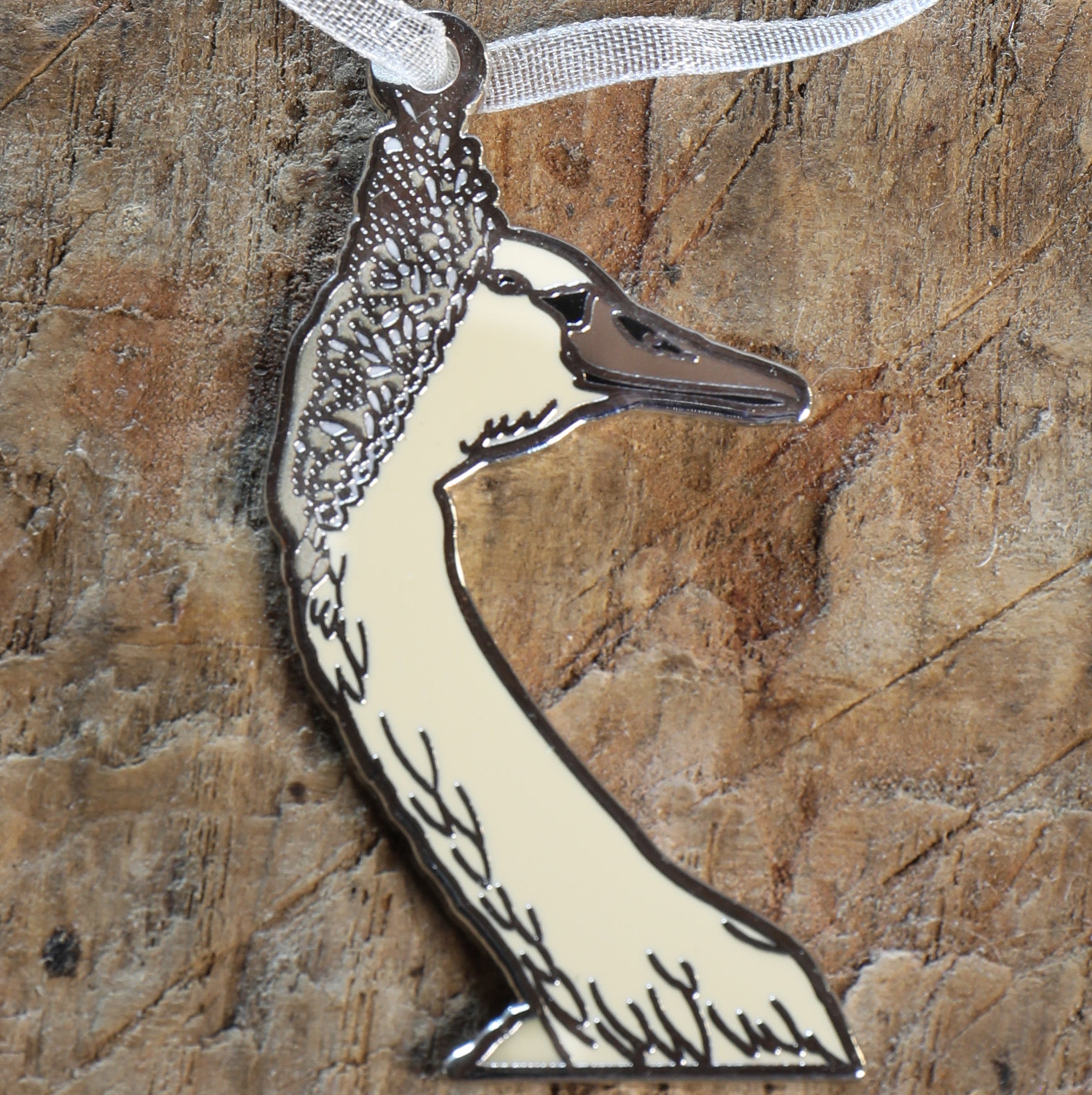 Swan shaped necklace with white organza ribbon on a textured wooden surface