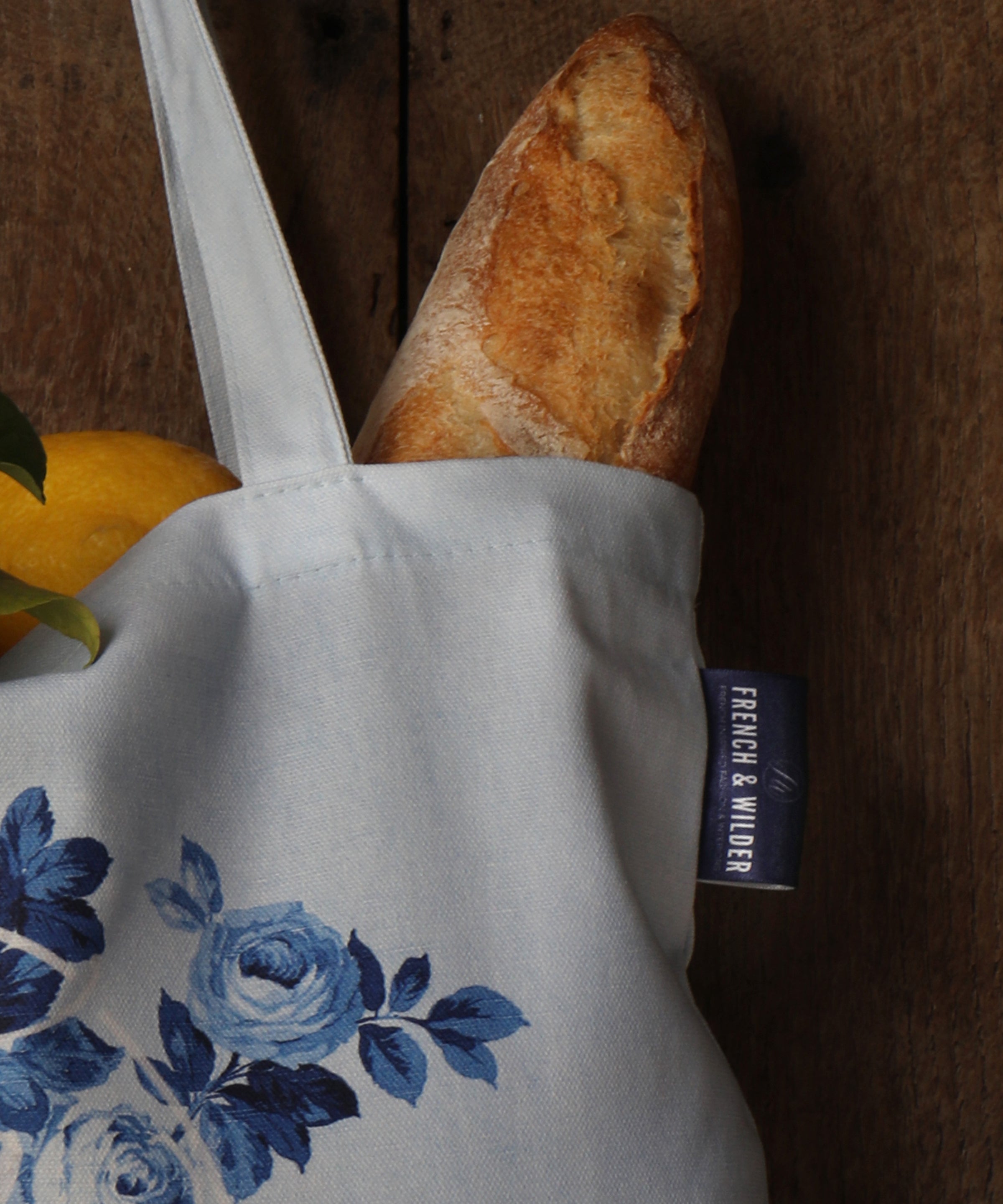 A close-up view of a blue floral pattern tote bag containing a baguette and lemons next to a wooden surface