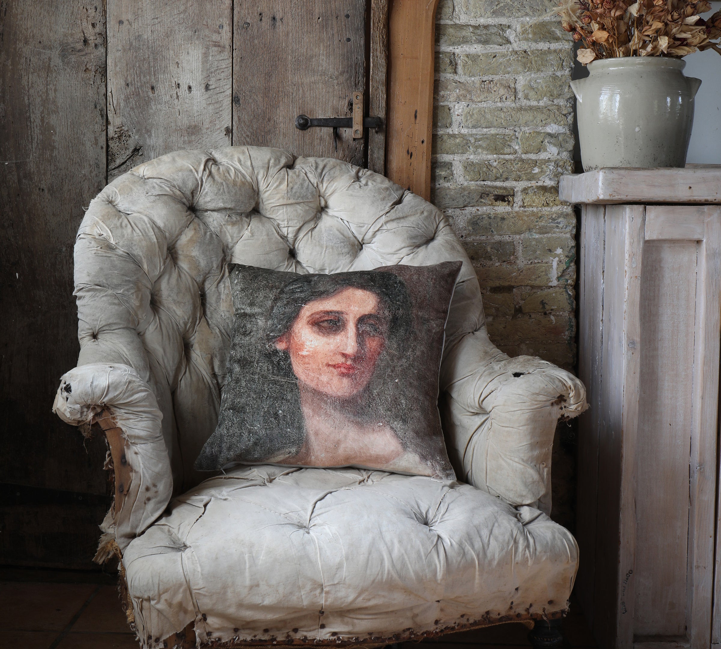 Velvet cushion with a design of a woman's portrait placed on a vintage chair in a a rustic setting