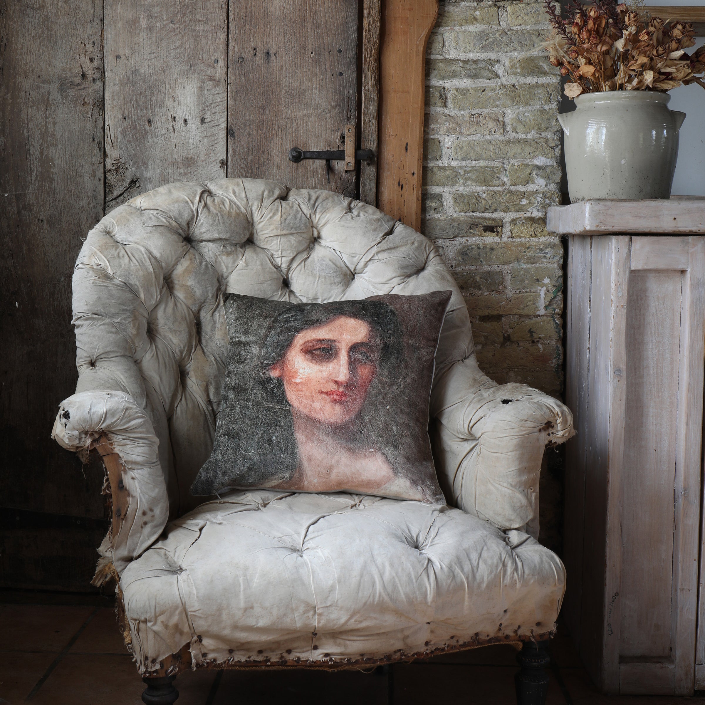 Velvet cushion with a design of a woman's portrait placed on a vintage chair in a a rustic setting